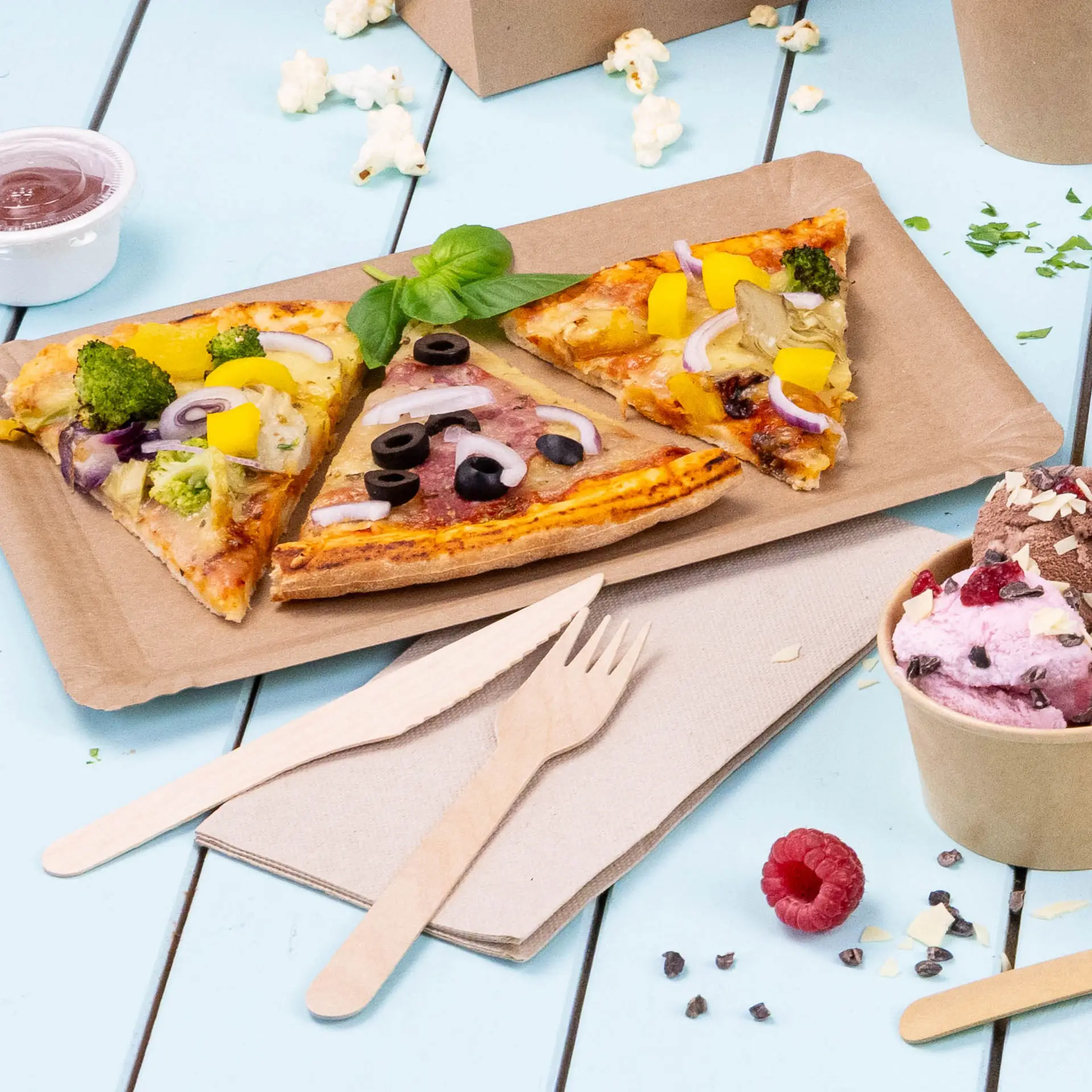 Obraz trzech kawałków pizzy na brązowej papierowej tacy, z drewnianymi sztućcami i kubkiem lodów w pobliżu.