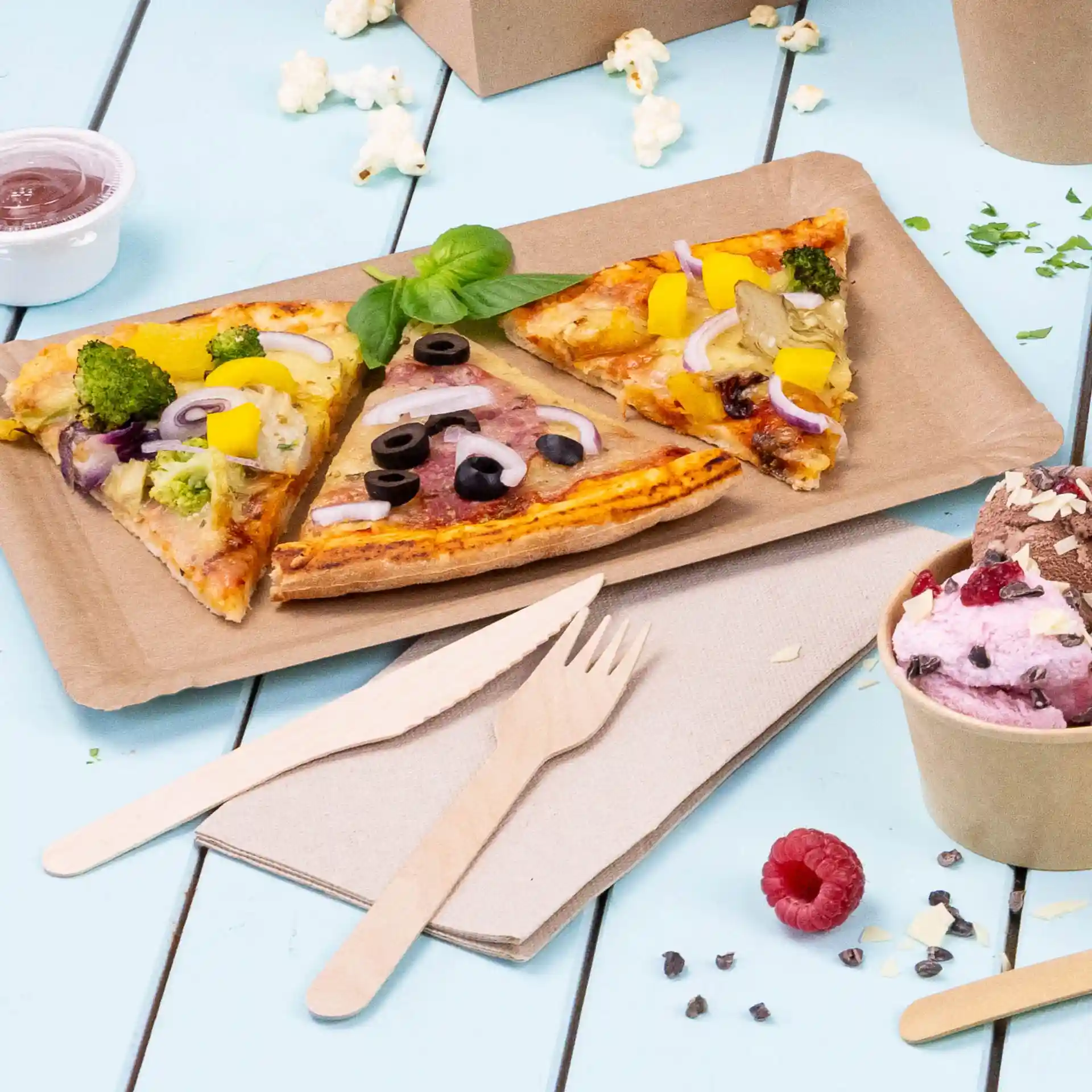 Obraz trzech kawałków pizzy na brązowej papierowej tacy, z drewnianymi sztućcami i kubkiem lodów w pobliżu.