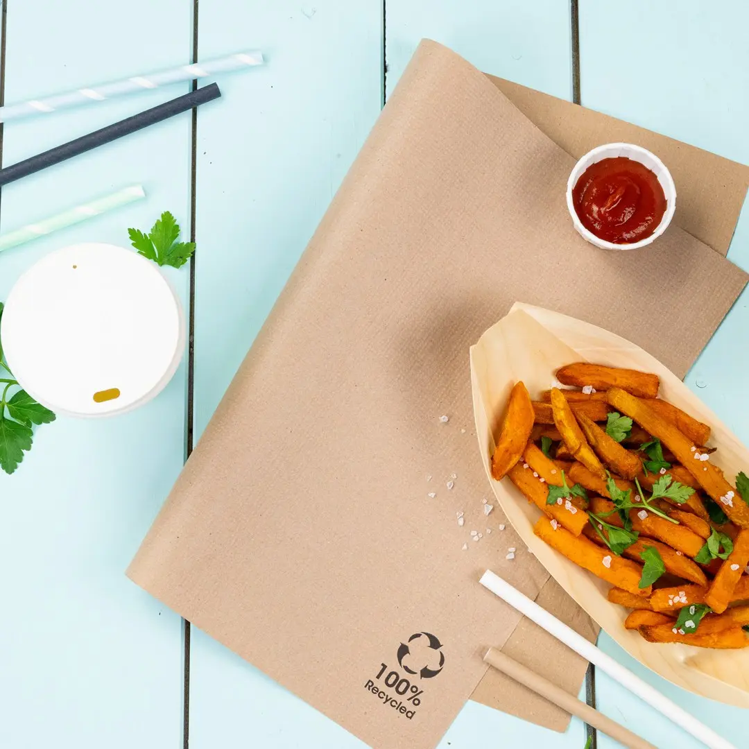 Brązowy papier kraft z frytkami z batatów, ketchupem, białym kubkiem i słomkami na niebieskiej drewnianej powierzchni.