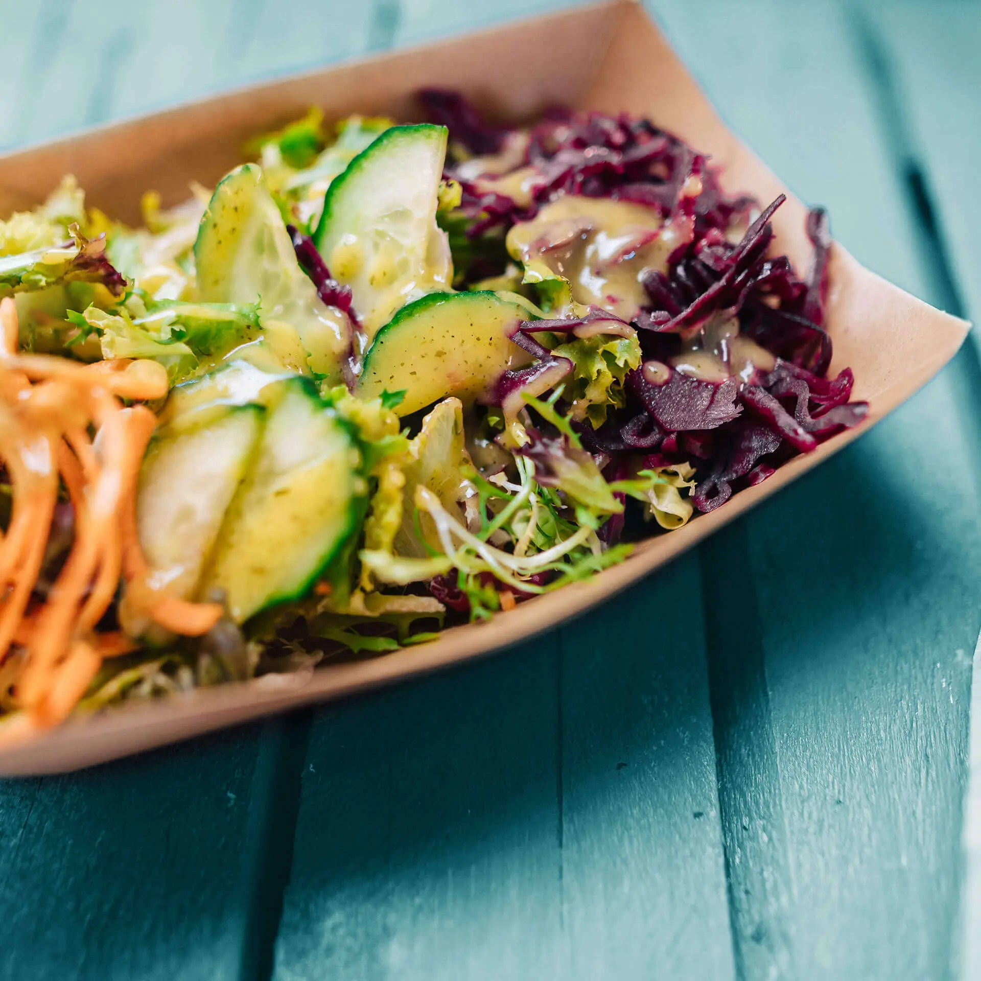 Miska na przekąski wypełniona sałatką mieszany, z plasterkami ogórka i startymi marchewkami, na zielonej drewnianej powierzchni.