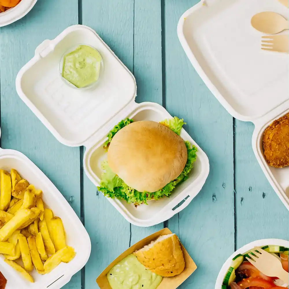 Jedno hamburger na sałacie w białym pojemniku na wynos, z frytkami, sosem do maczania i dodatkowymi jedzeniem widocznym.