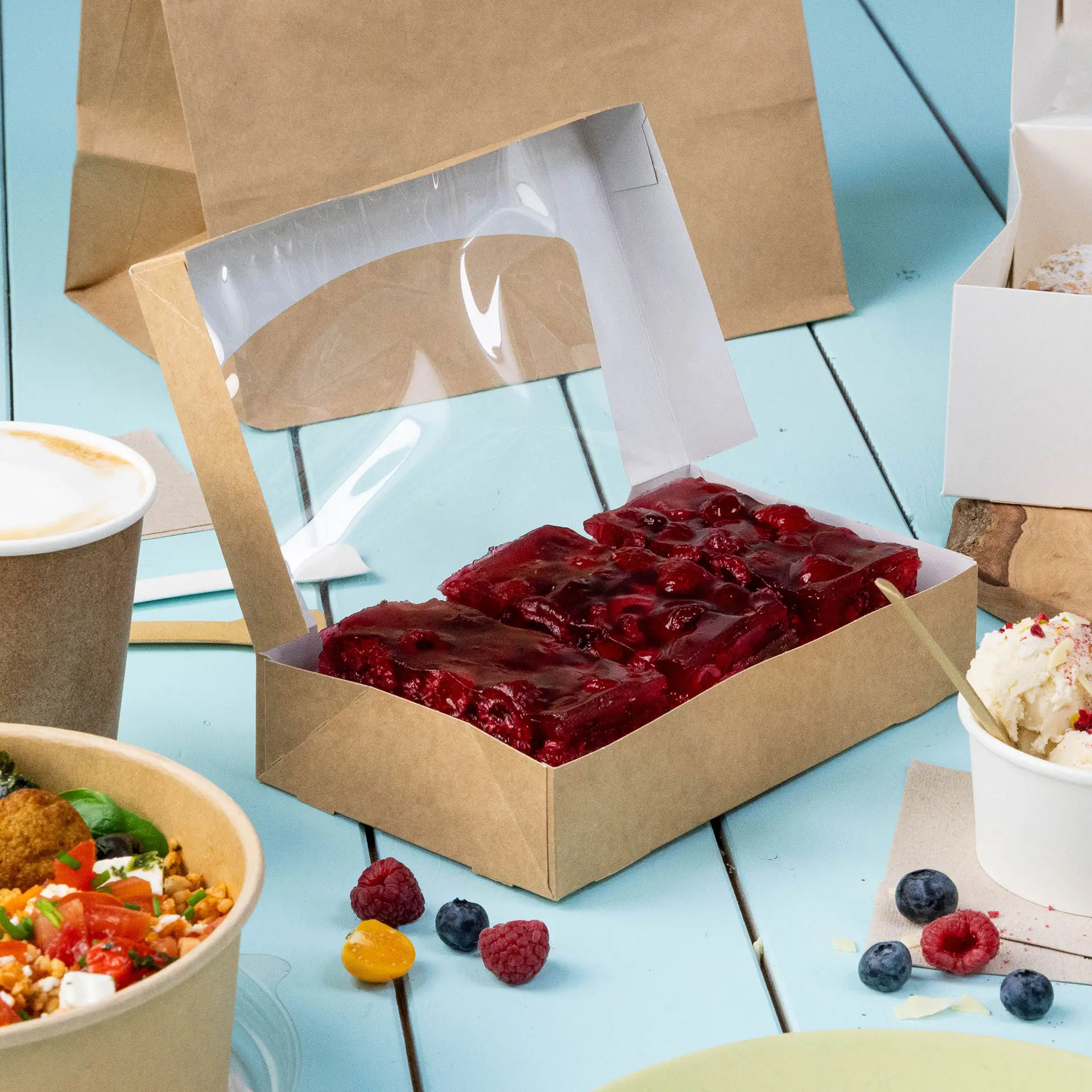 Jedna pudełko tekturowe z oknem z przezroczystym wiekiem z celulozy, zawierające czerwone ciastka, na niebieskim tle z dodatkowymi produktami spożywczymi.