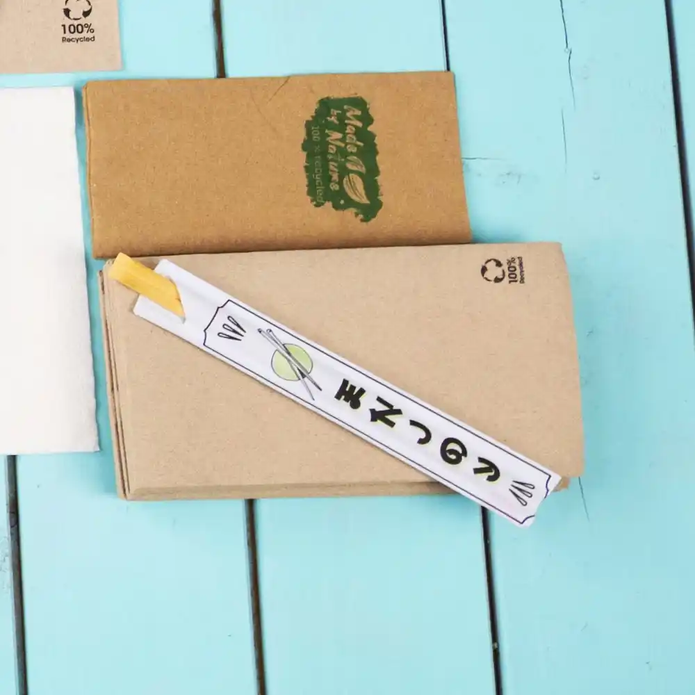 Pałeczki owinięte w papier na niebieskiej drewnianej powierzchni, z brązowym pudełkiem kraftowym w tle.