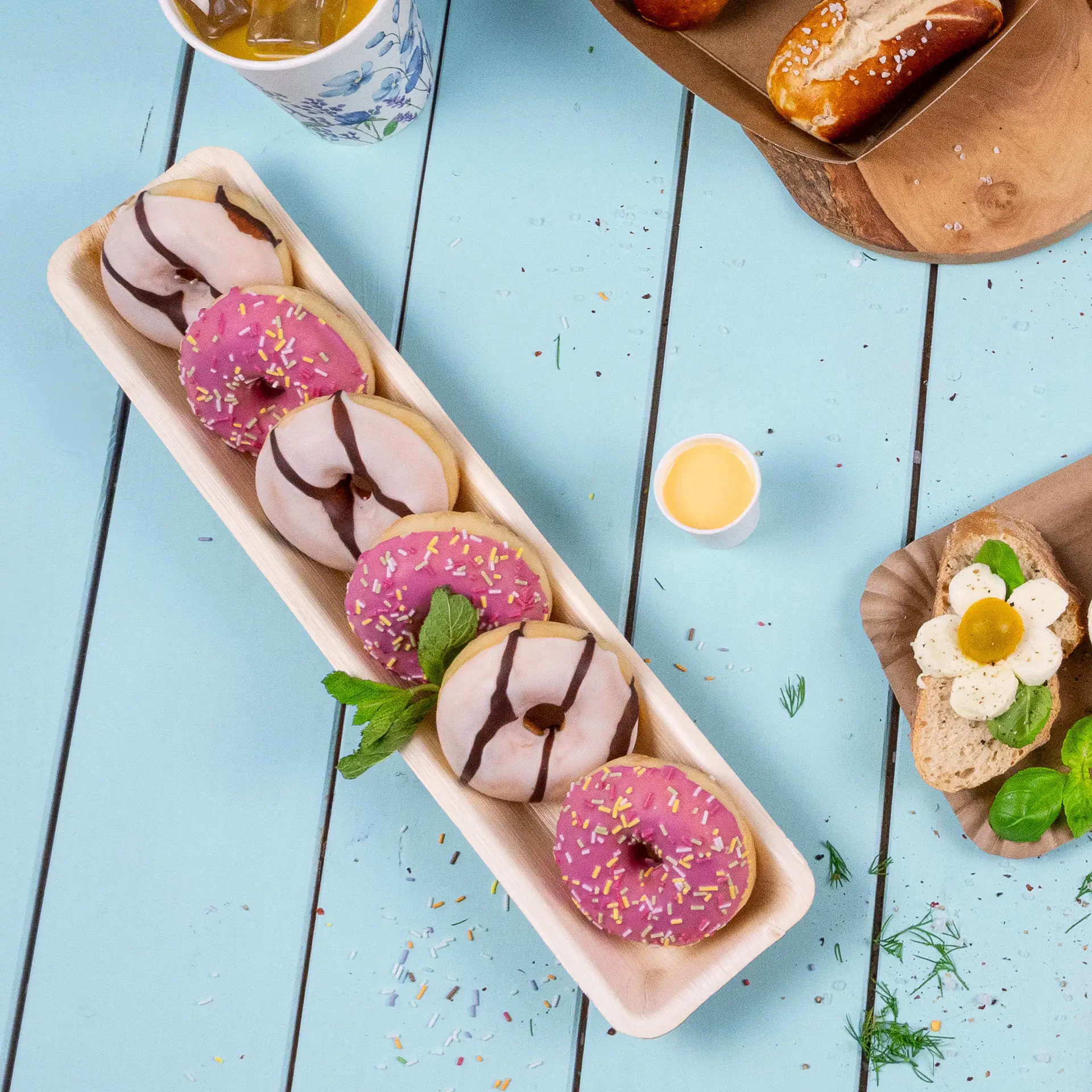 Prostokątny tacę z liści palmowych z kilkoma ozdobionymi pączkami; różowa i biała polewa ze sprinkles.