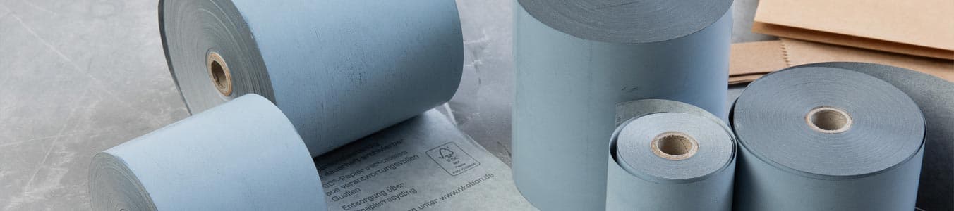 Różne rolki niebieskiego papieru w różnych rozmiarach, z arkuszem brązowego papieru widocznym w tle.