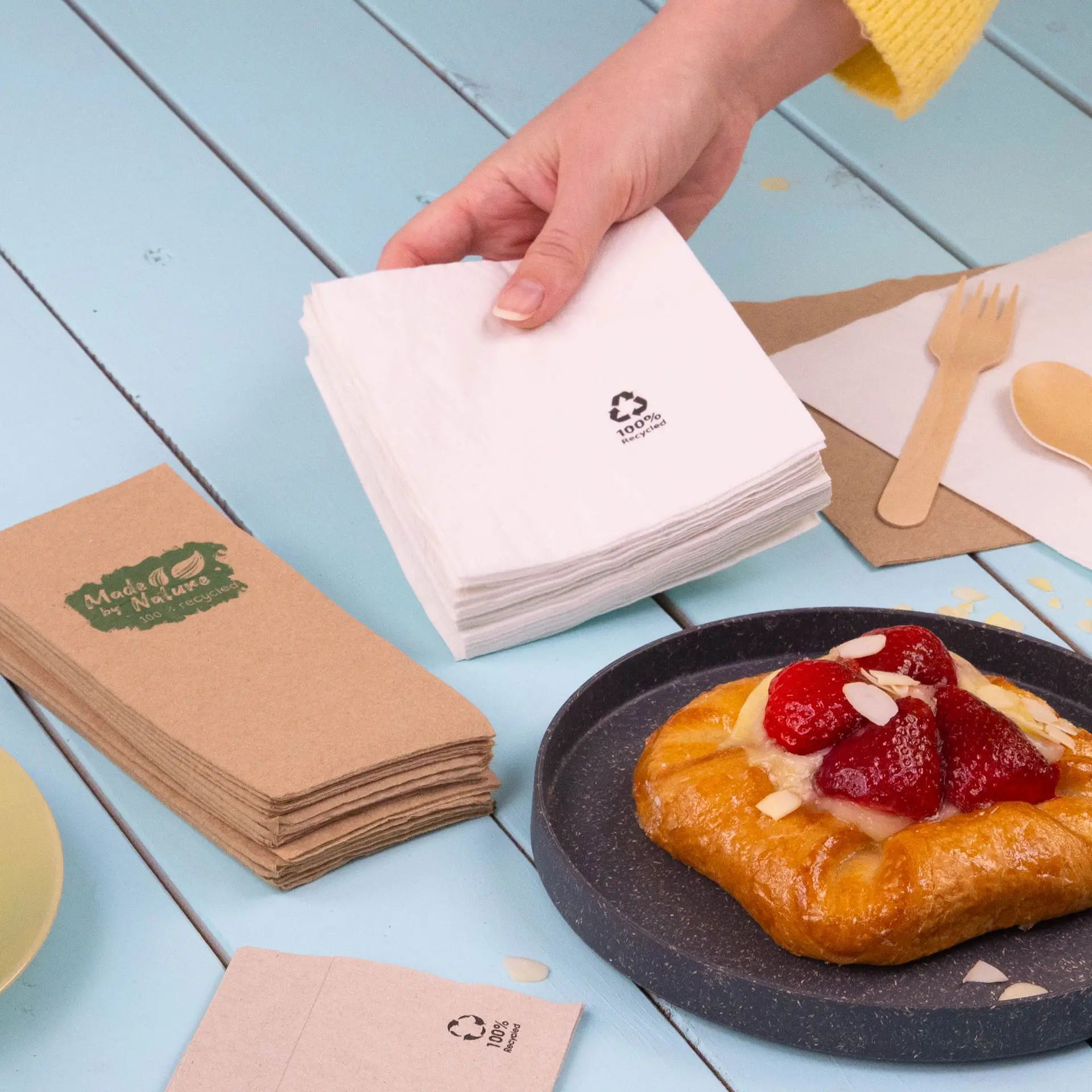 Dwie kwadratowe serwetki koktajlowe, jedna biała i jedna jasnoszara, wykonane z papieru z recyklingu, z symbolami recyklingu.