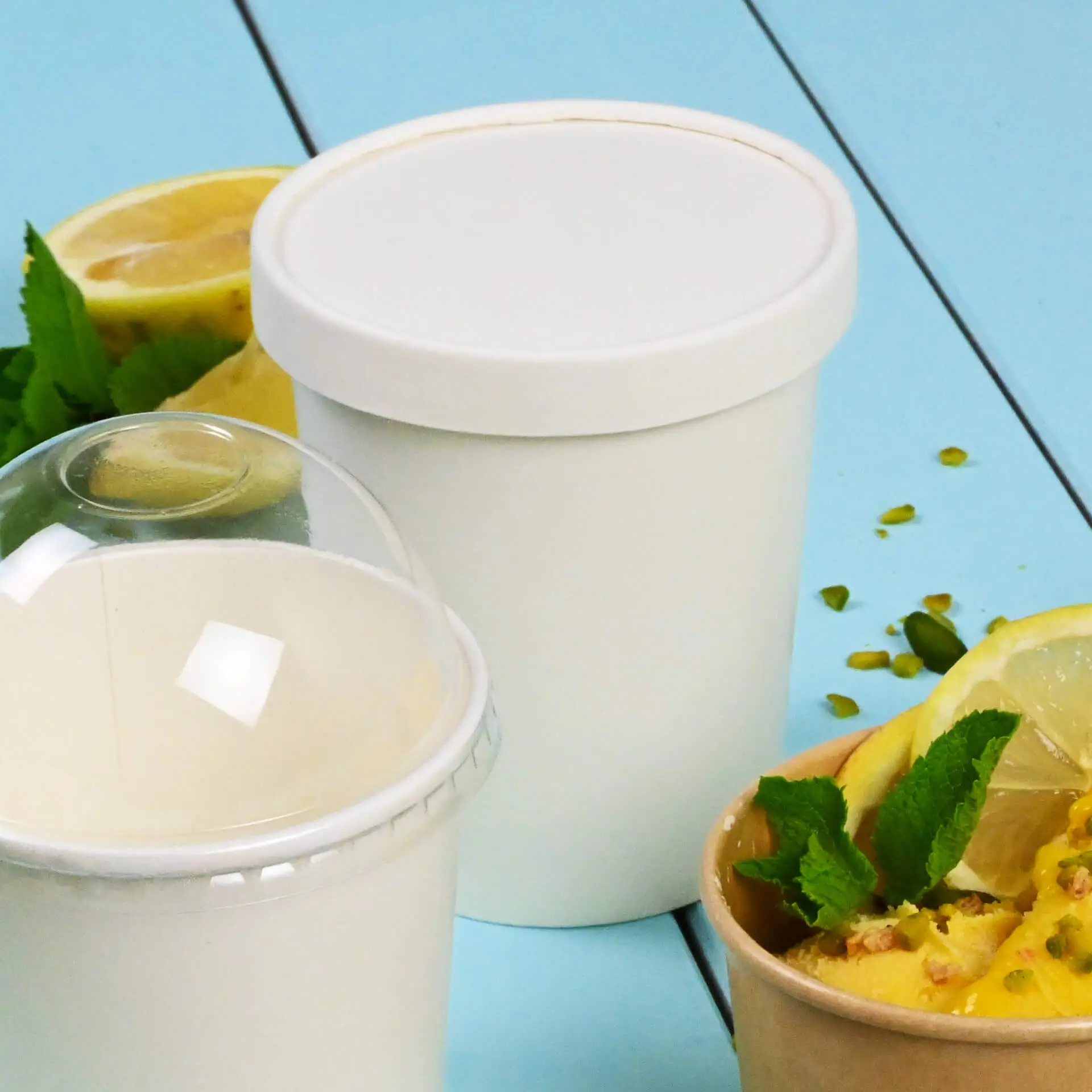 Biały kartonowy dekiel do pucharków lodowych, pokazany z plasterkami cytryny i miętą; dodatkowy pojemnik na lody na pierwszym planie.