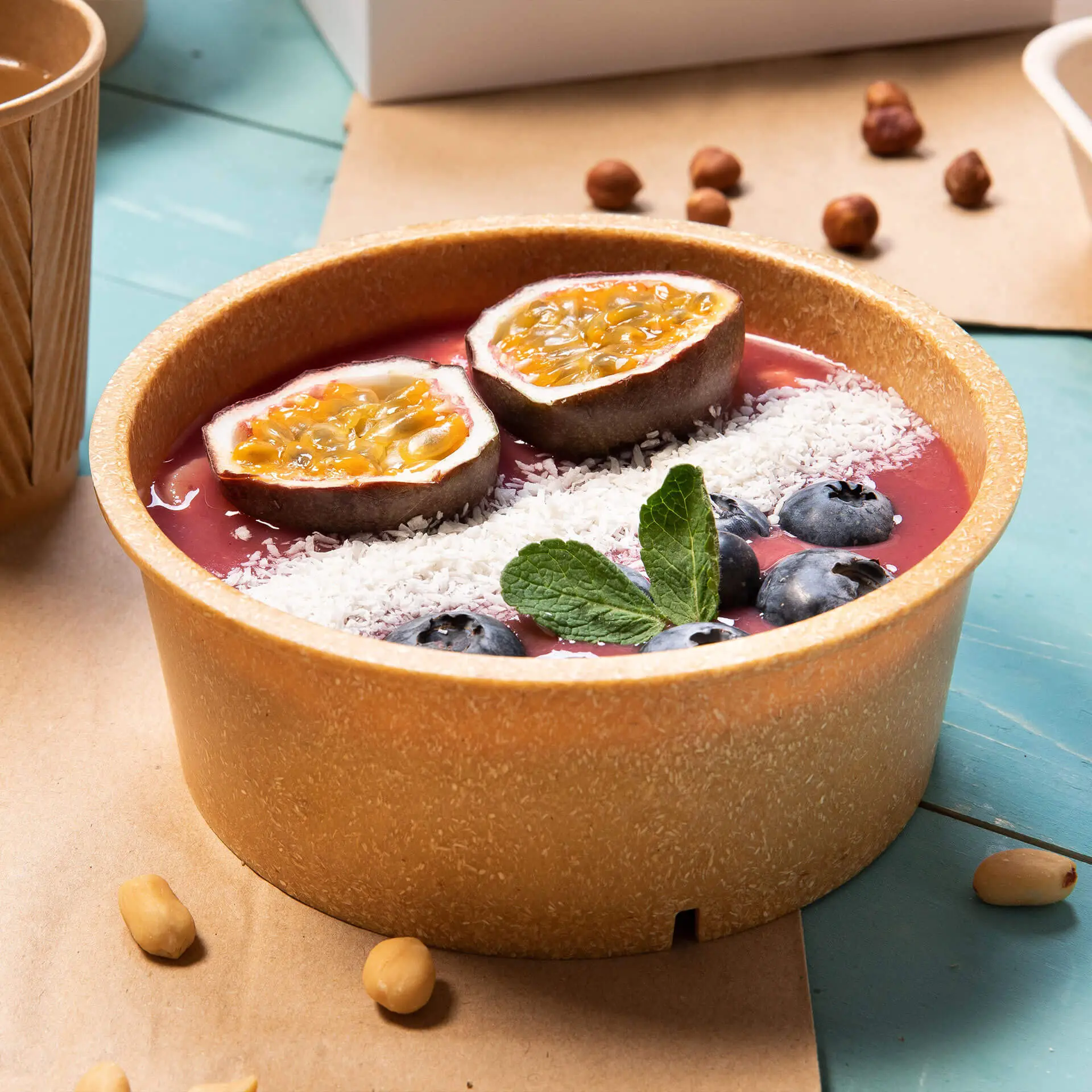 Wielokrotnego użytku brązowa miska wypełniona różowym smoothie, udekorowana połówkami owoców marakui, wiórkami kokosu, borówkami i miętą.