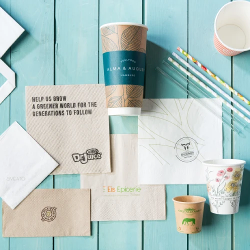 Brązowe i białe serwetki papierowe, jednorazowe kubki i słomki na niebieskiej drewnianej powierzchni.