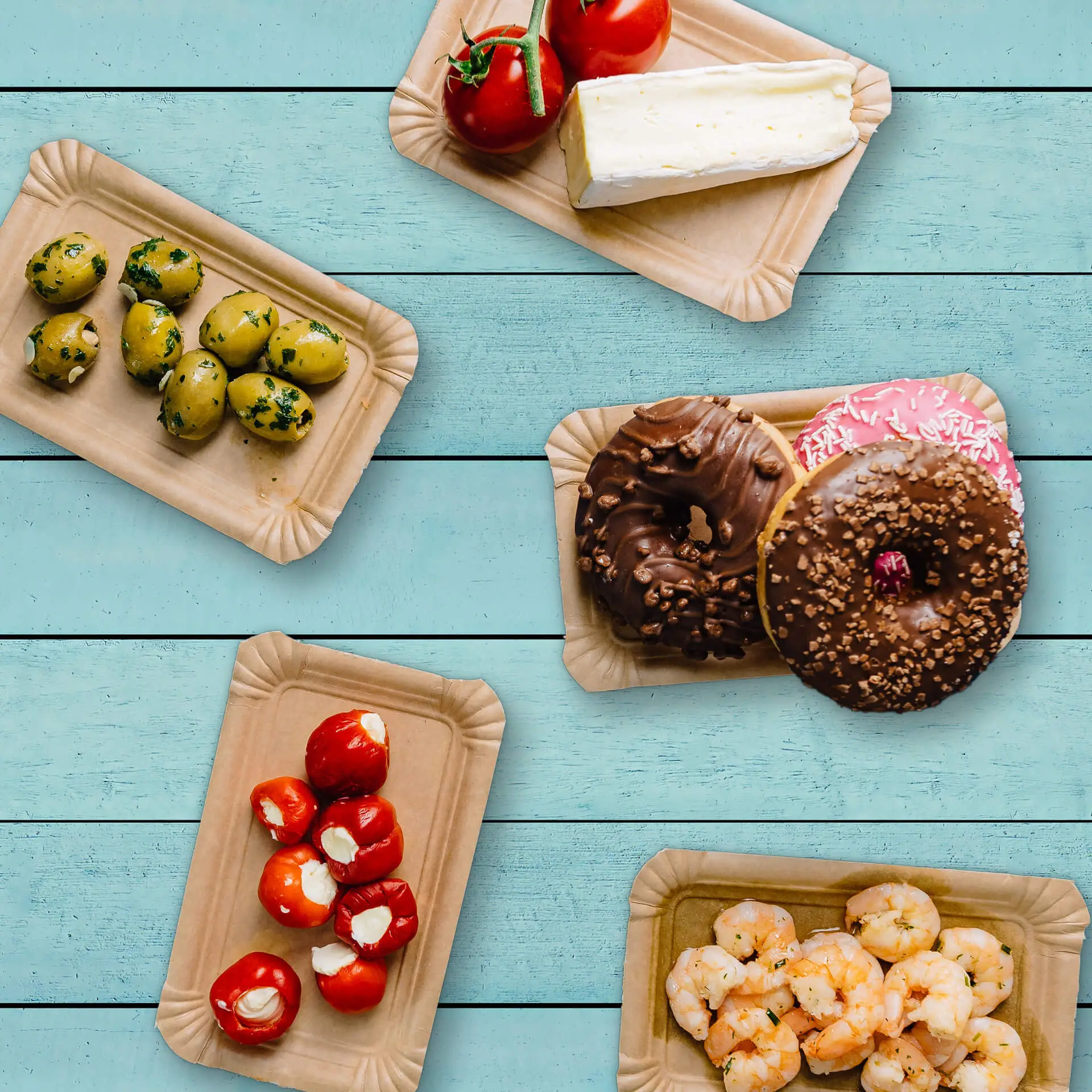 Talerze tekturowe z różnymi potrawami: oliwki, pomidory, ser, krewetki i pączki, ułożone na jasnoniebieskim tle.