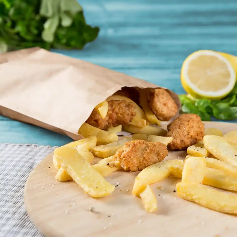 Papierowa torba z frytkami i kilkoma złotobrązowymi kawałkami, z cytryną i zielenią w tle.