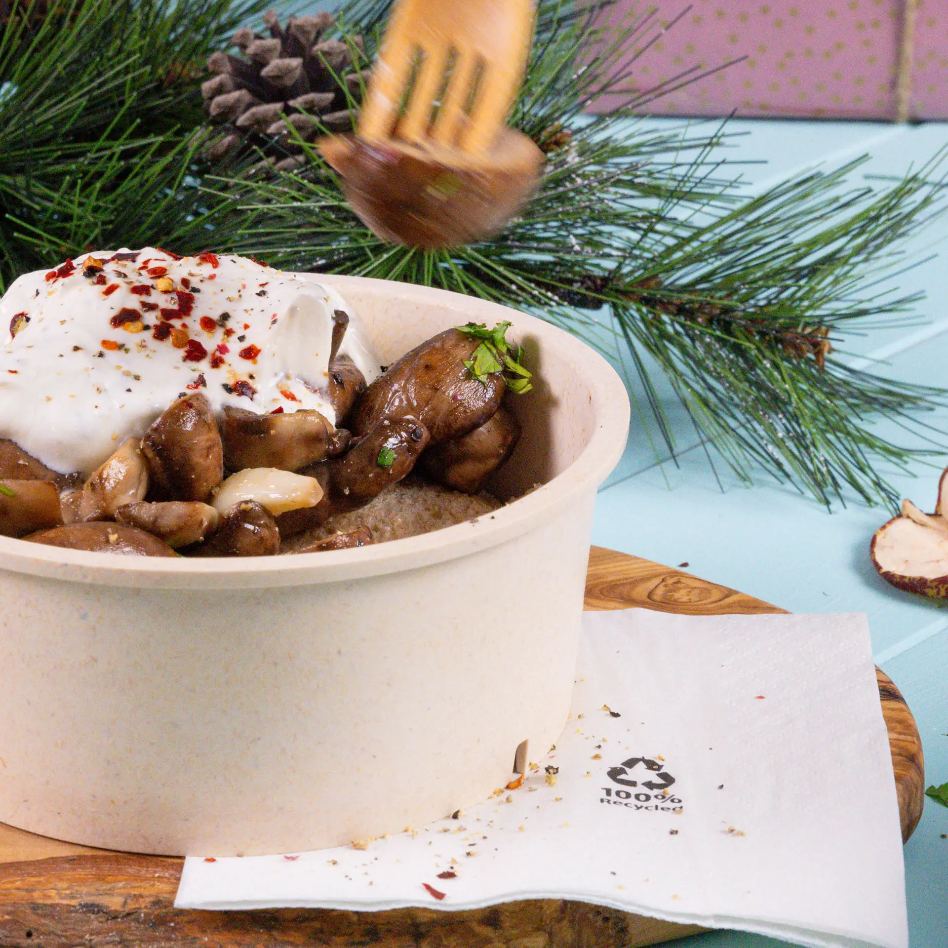 Jedna zrównoważona miska mieszanych grzybów, posypana jogurtem i płatkami chili, z drewnianym widelcem podnoszącym kawałek; serwetka poniżej.