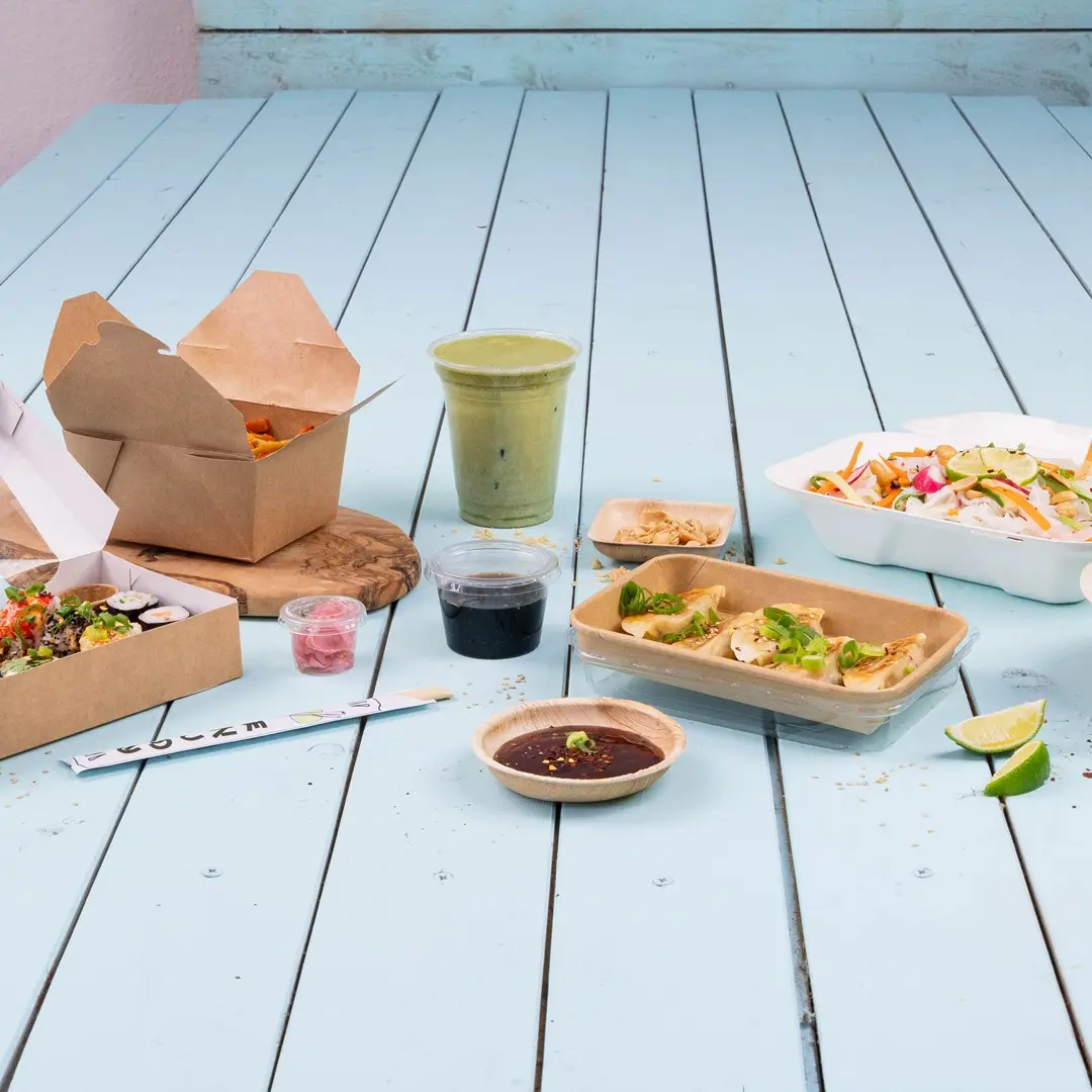 Różnorodne azjatyckie jedzenie na niebieskim drewnianym stole, w tym sushi, pierożki, sałatka i zielony napój.