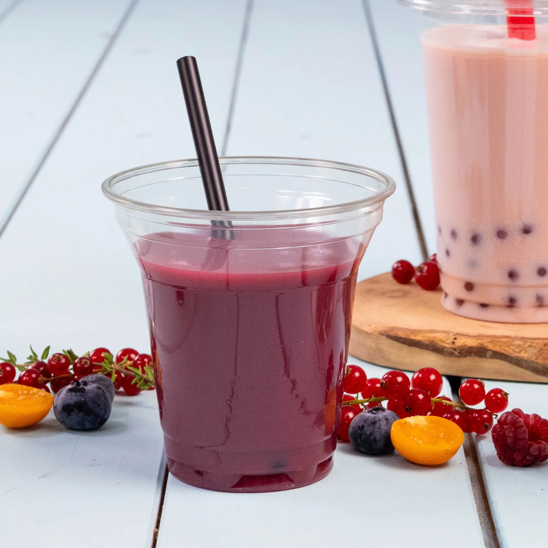 Przezroczysty kubek wypełniony ciemnoczerwonym sokiem i czarną słomką; ozdobiony jagodami i pół żółtego owocu.