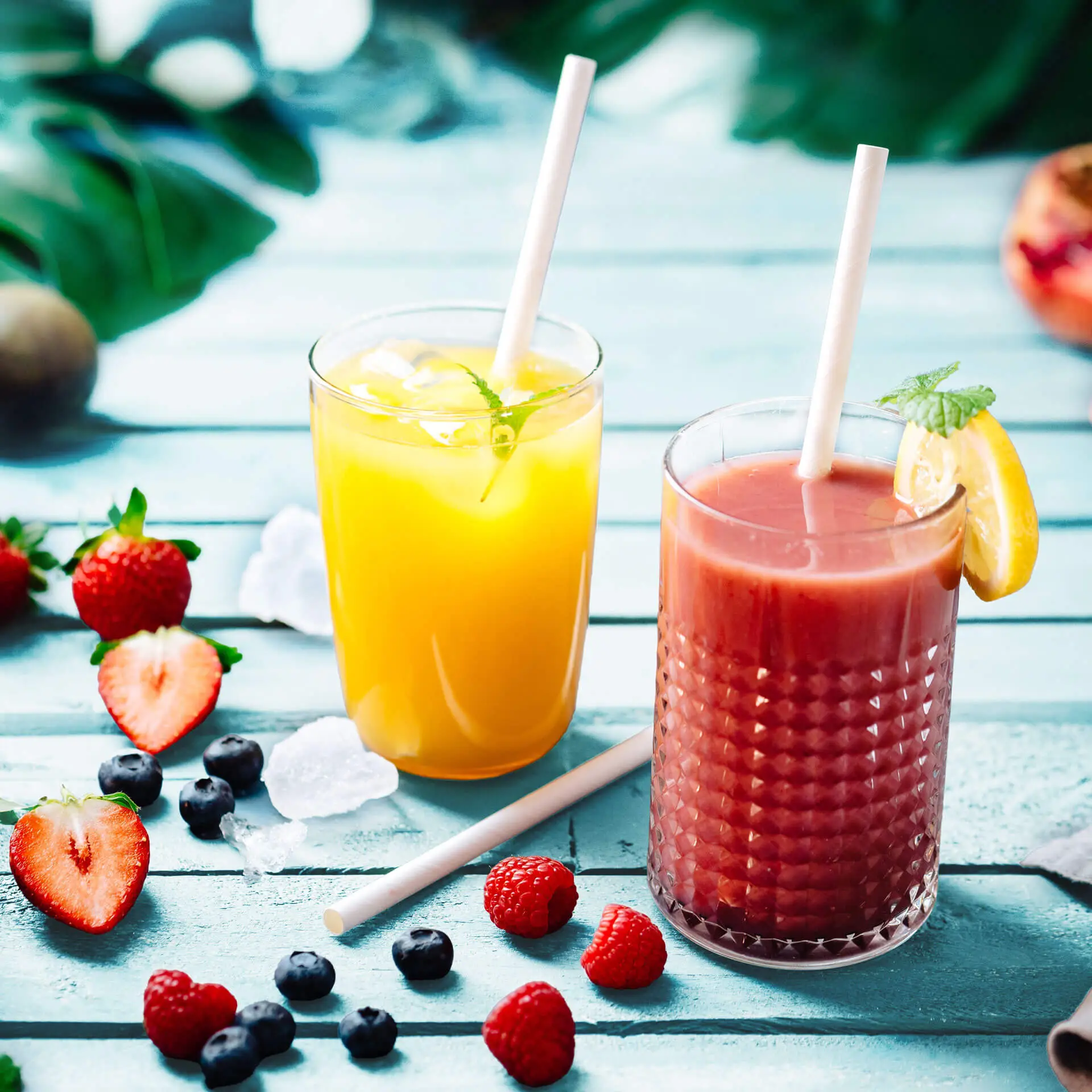 Dwa napoje w przezroczystych szklankach z białymi jumbo papierowymi słomkami; jeden żółty napój z miętą i lodem, jeden czerwonawy napój z plasterkiem cytryny.