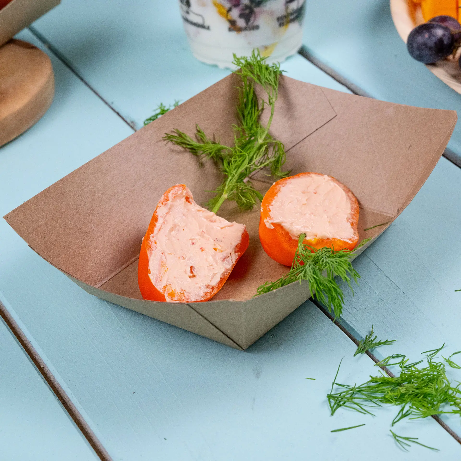 Talerz na przekąski z kartonu odpornego na tłuszcz z dwiema połówkami pomarańczy wypełnionymi pastą, udekorowanymi świeżymi ziołami.