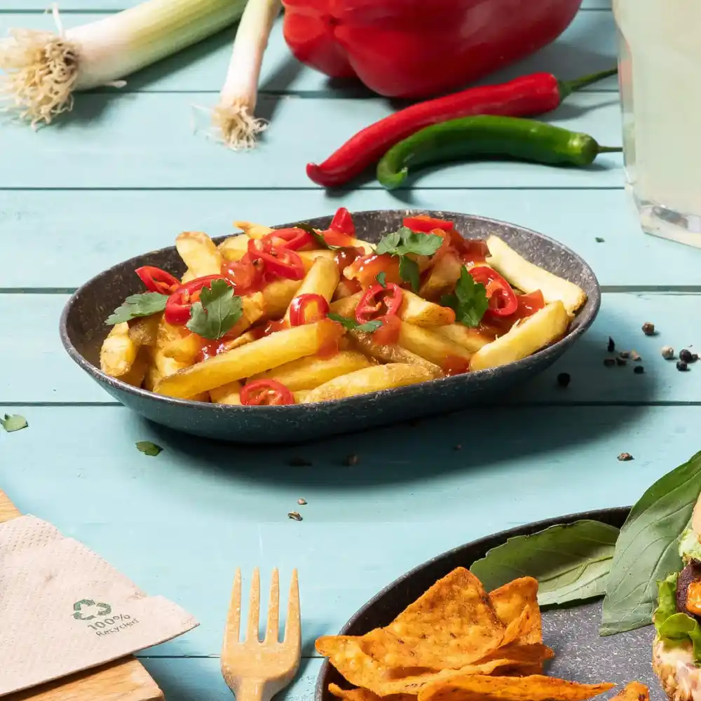 Miska frytek, posypana pokrojoną papryczką chili i kolendrą na niebieskim drewnianym stole.