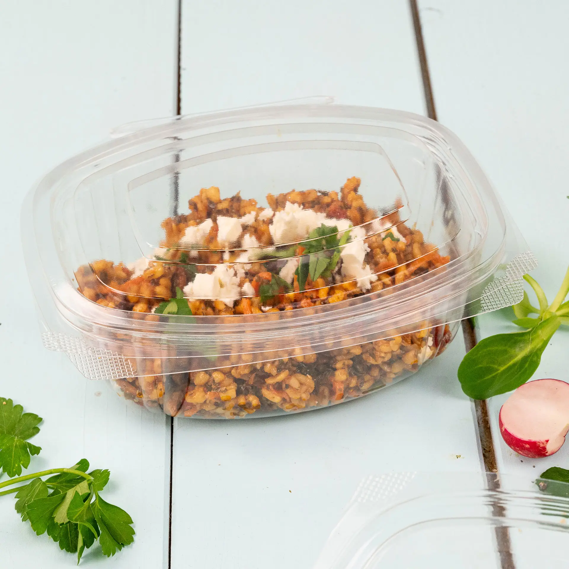 Miska Deli zawierająca zimne danie z warzywami i ziołami, z biodegradowalnego plastiku PLA, na niebieskim stole.