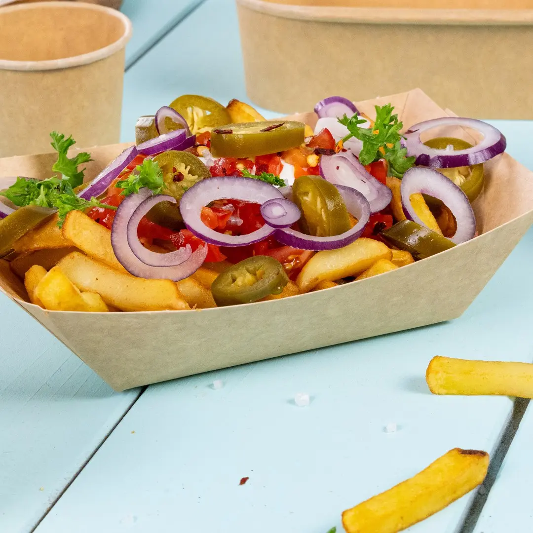 Miska frytek z pokrojoną cebulą, jalapeños, pokrojonymi pomidorami i pietruszką na niebieskiej powierzchni.