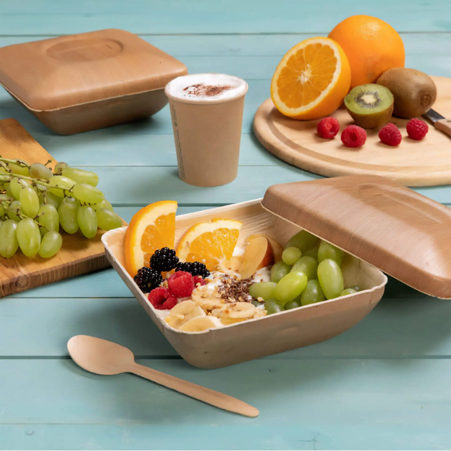 Jedna kwadratowa miseczka z liści palmowych z pokrywką wypełniona owocami; zawiera zielone winogrona, plastry pomarańczy, maliny i jeżyny.