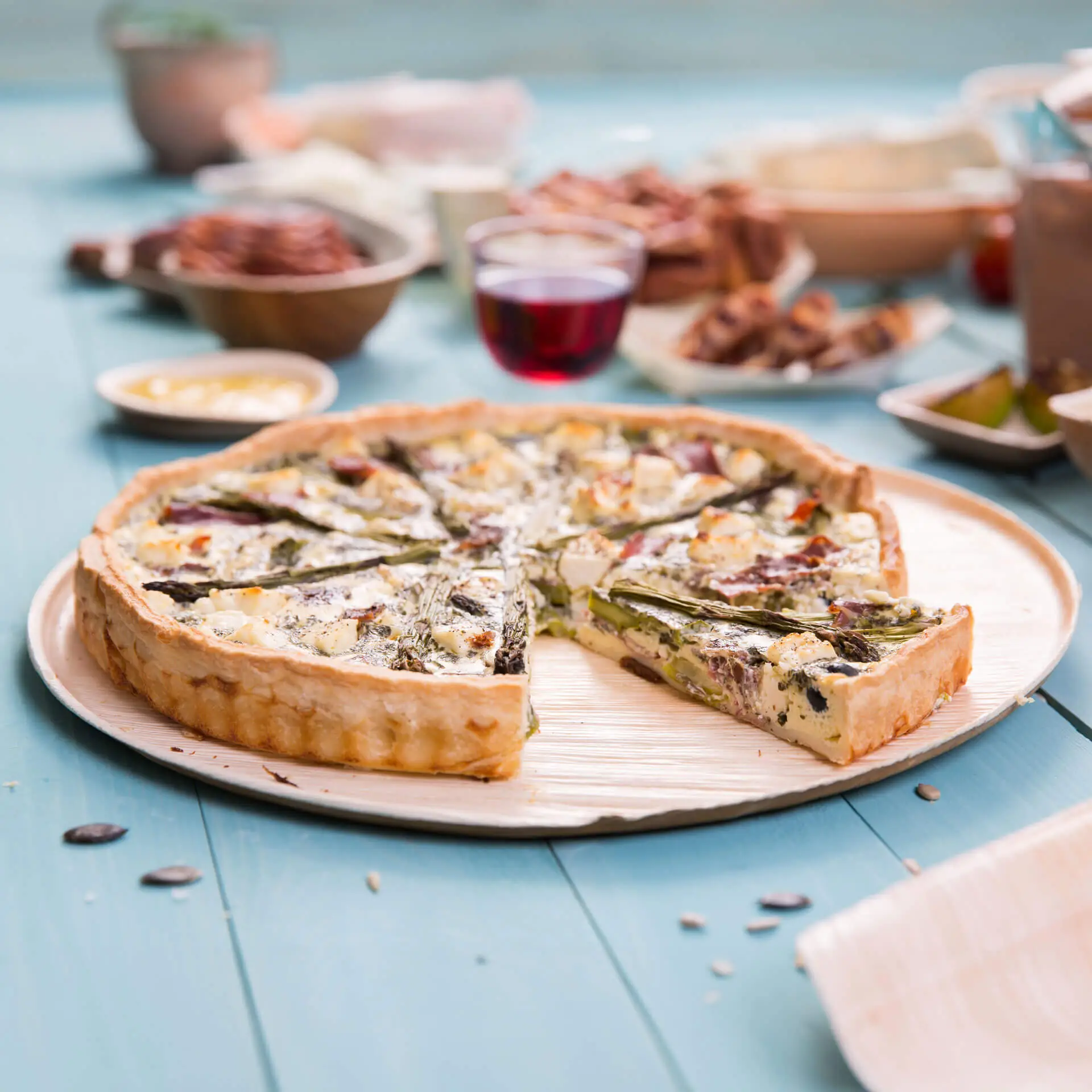 Okrągły talerz do pizzy z liścia palmy z wyjętym kawałkiem; otoczony różnymi potrawami i napojem na drewnianym stole.