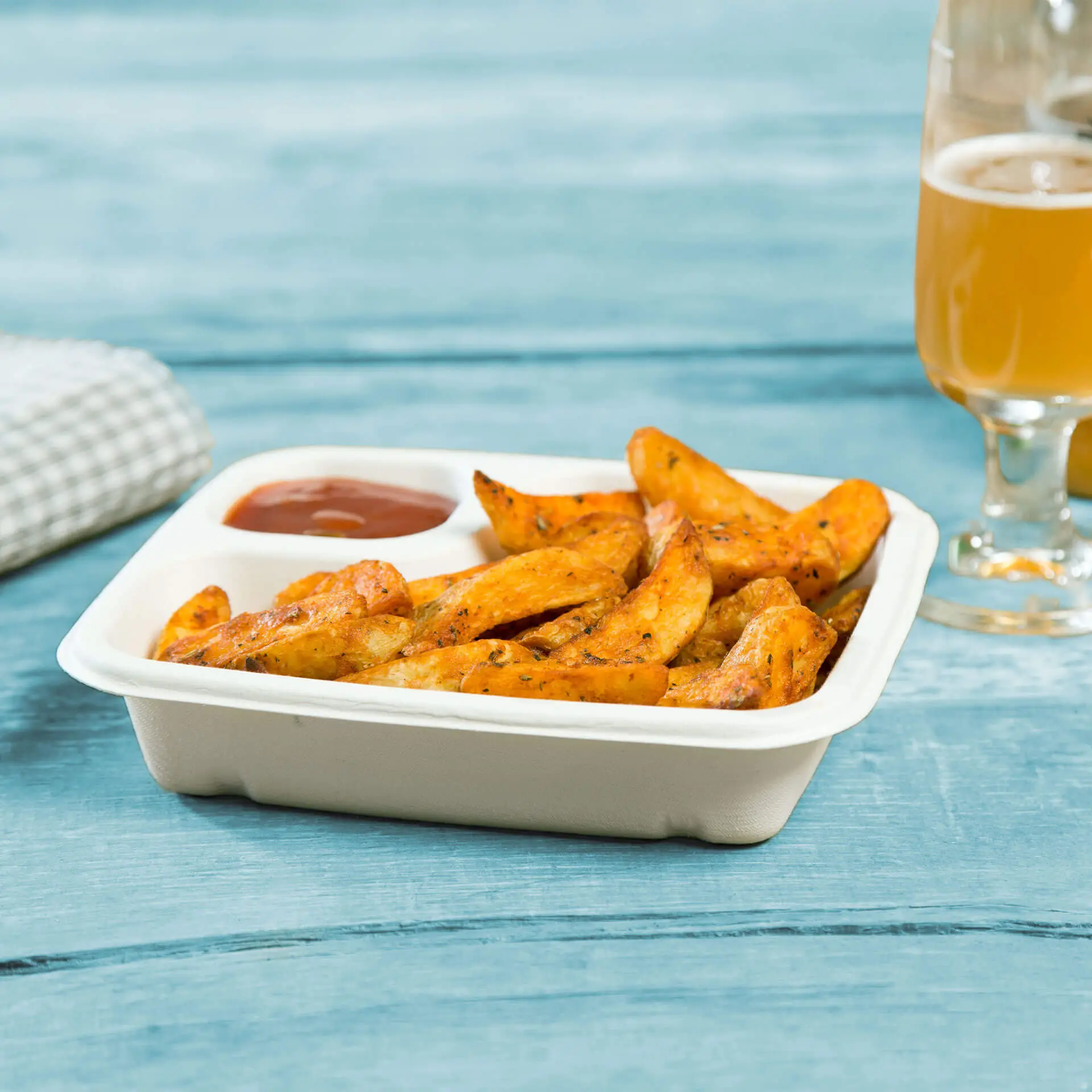 Chrupiące kawałki ziemniaków podane w biodegradowalnym talerzu z trzciny cukrowej z sosem z boku.