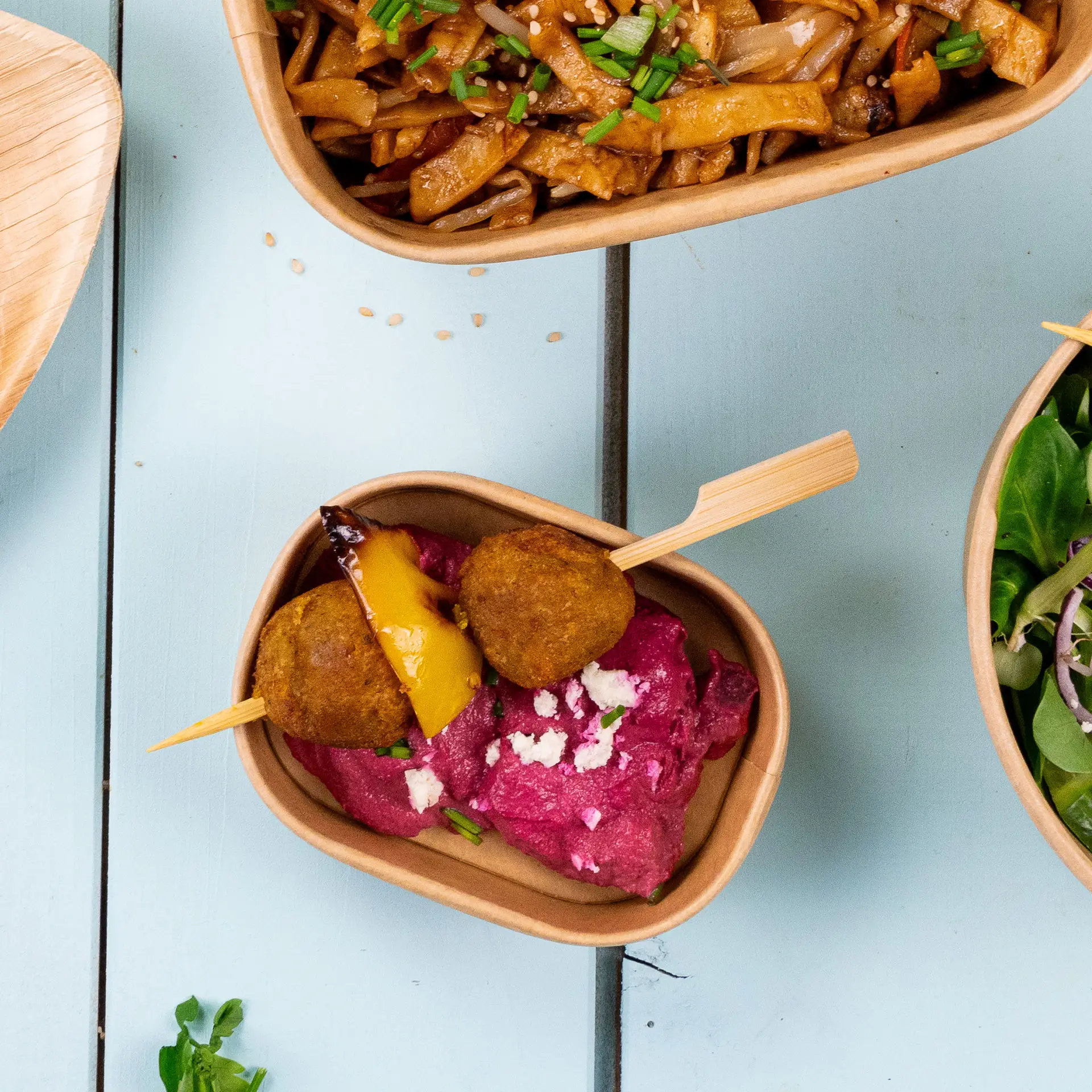 Bambozowy szpikulec z dwiema złotymi kulkami i kawałkiem żółtej papryki na różowym puree w brązowej misce.