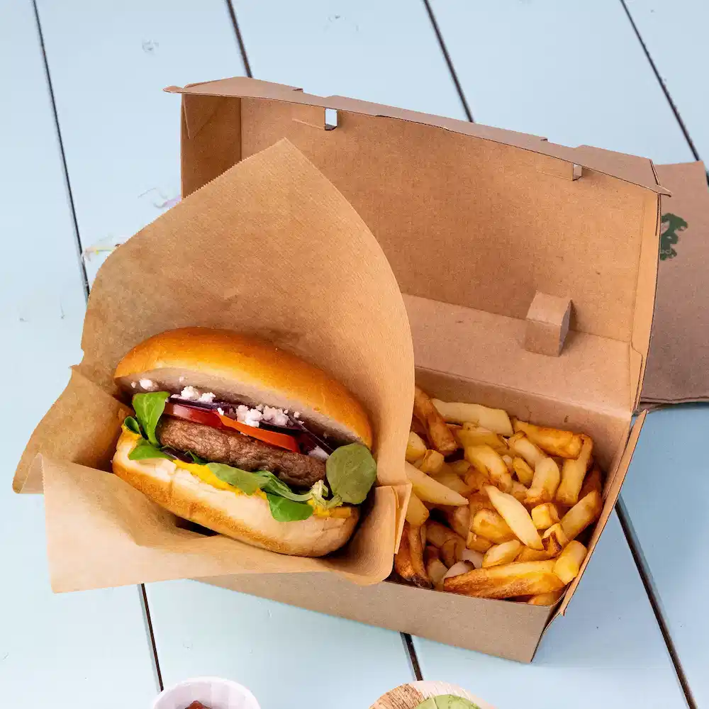 Burger z dodatkami umieszczony w pudełku na wynos obok porcji frytek.