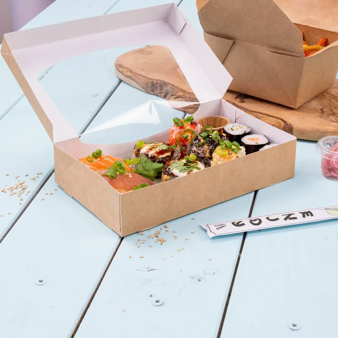 Pudełko sushi z różnymi rolkami sushi, łososiem i dodatkami, umieszczone na jasnoniebieskiej drewnianej powierzchni.