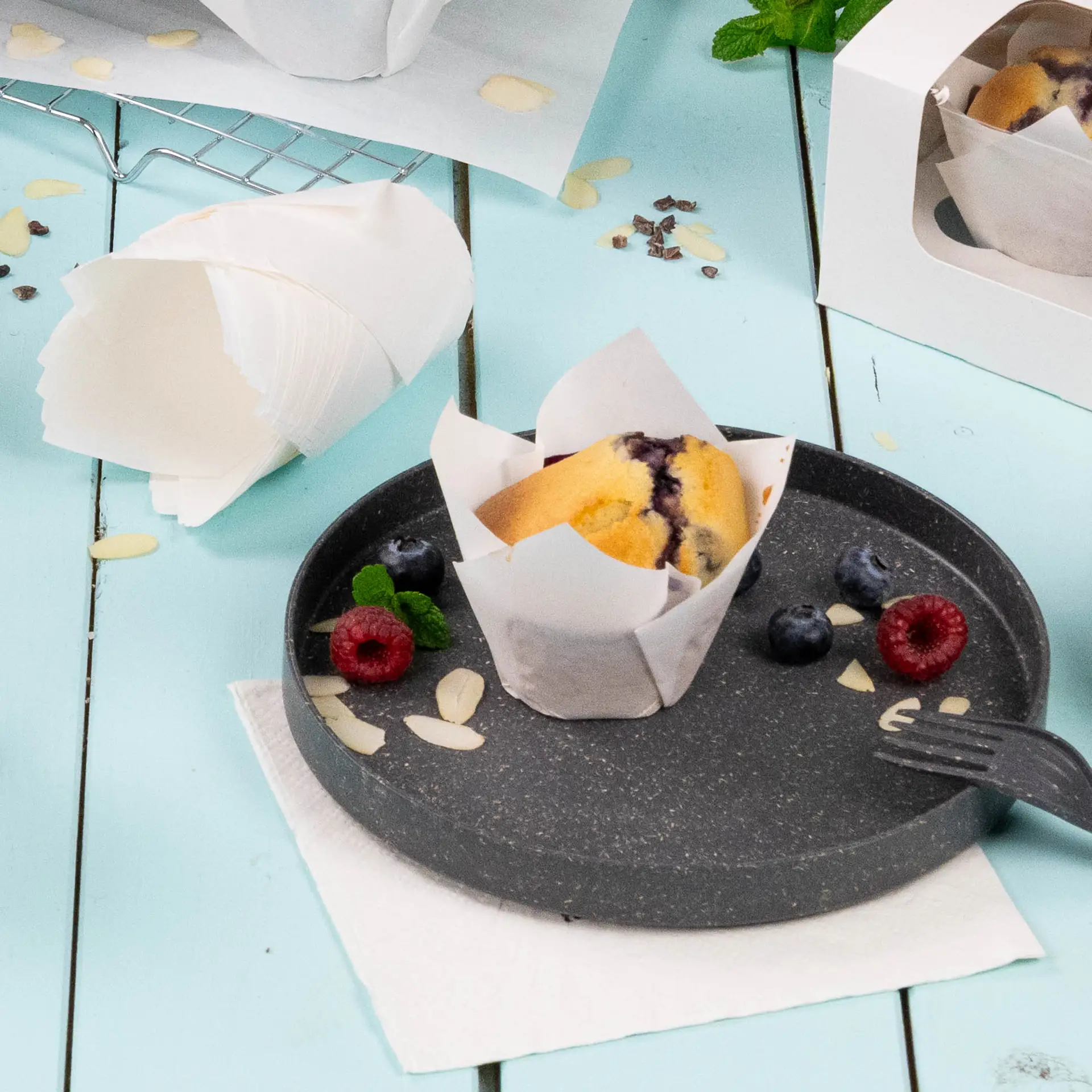 Biały kubek muffinowy z papierem odporowym na tłuszcz na ciemnym talerzu; udekorowany malinami, borówkami i plasterkami migdałów.