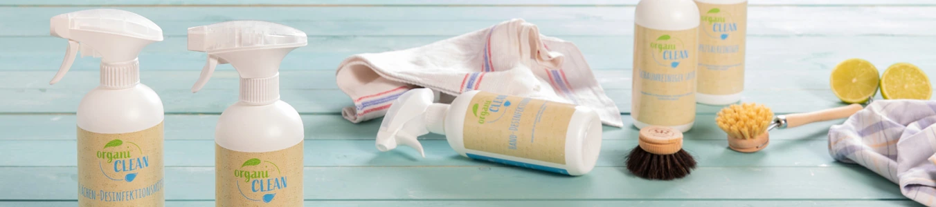 Dwie butelki spray z płynem czyszczącym z etykietami, ściereczka, szczotka i przekrojone limonki na niebieskiej drewnianej powierzchni.