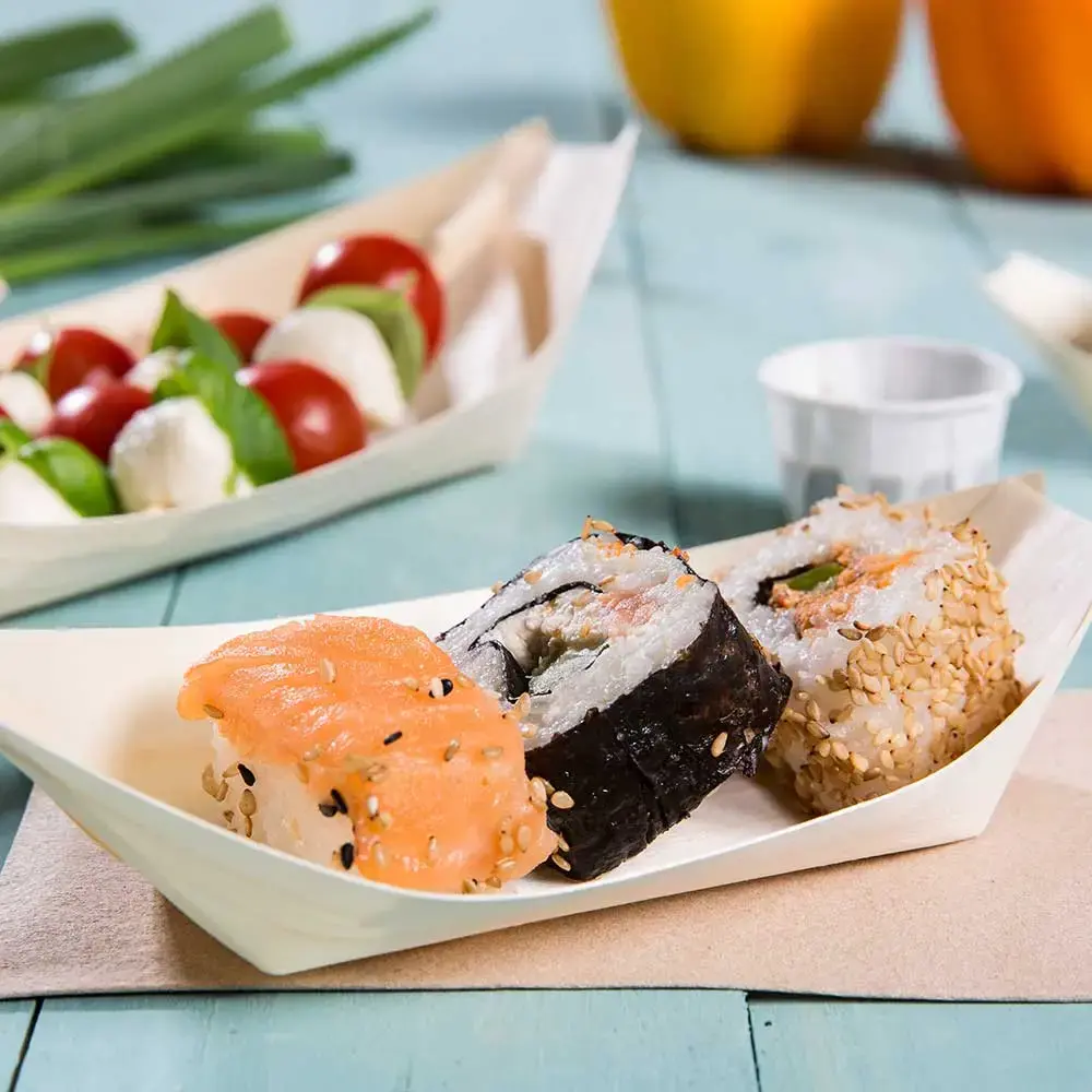 Rolki sushi podane w drewnianym naczyniu w kształcie łodzi, z łososiem, sezamem i nori, z dodatkiem pomidorków koktajlowych i mozzarelli.