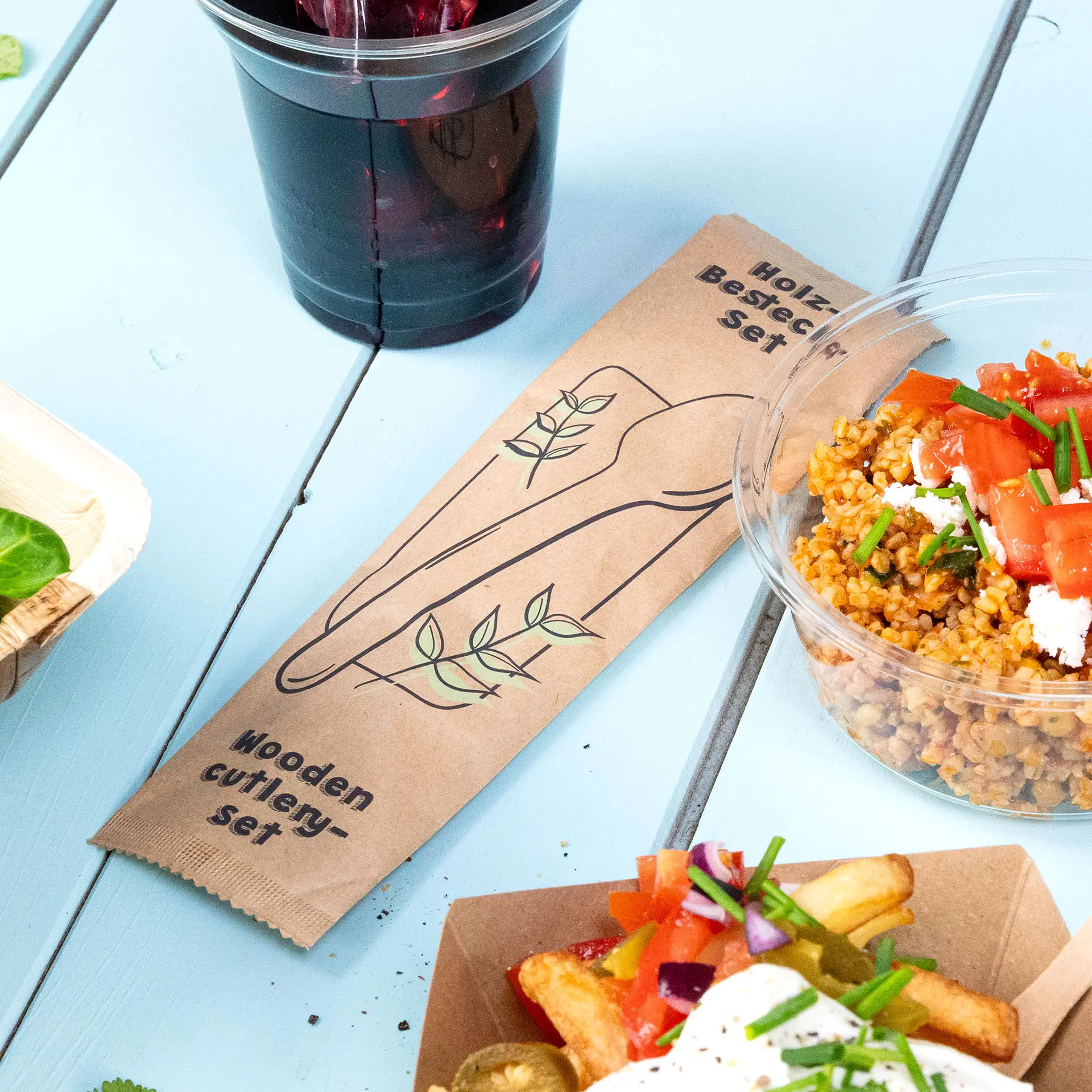 Drewniany zestaw sztućców z łyżką i serwetką na widoku; zawiera biodegradowalny worek i nadaje się do gorących lub zimnych potraw.