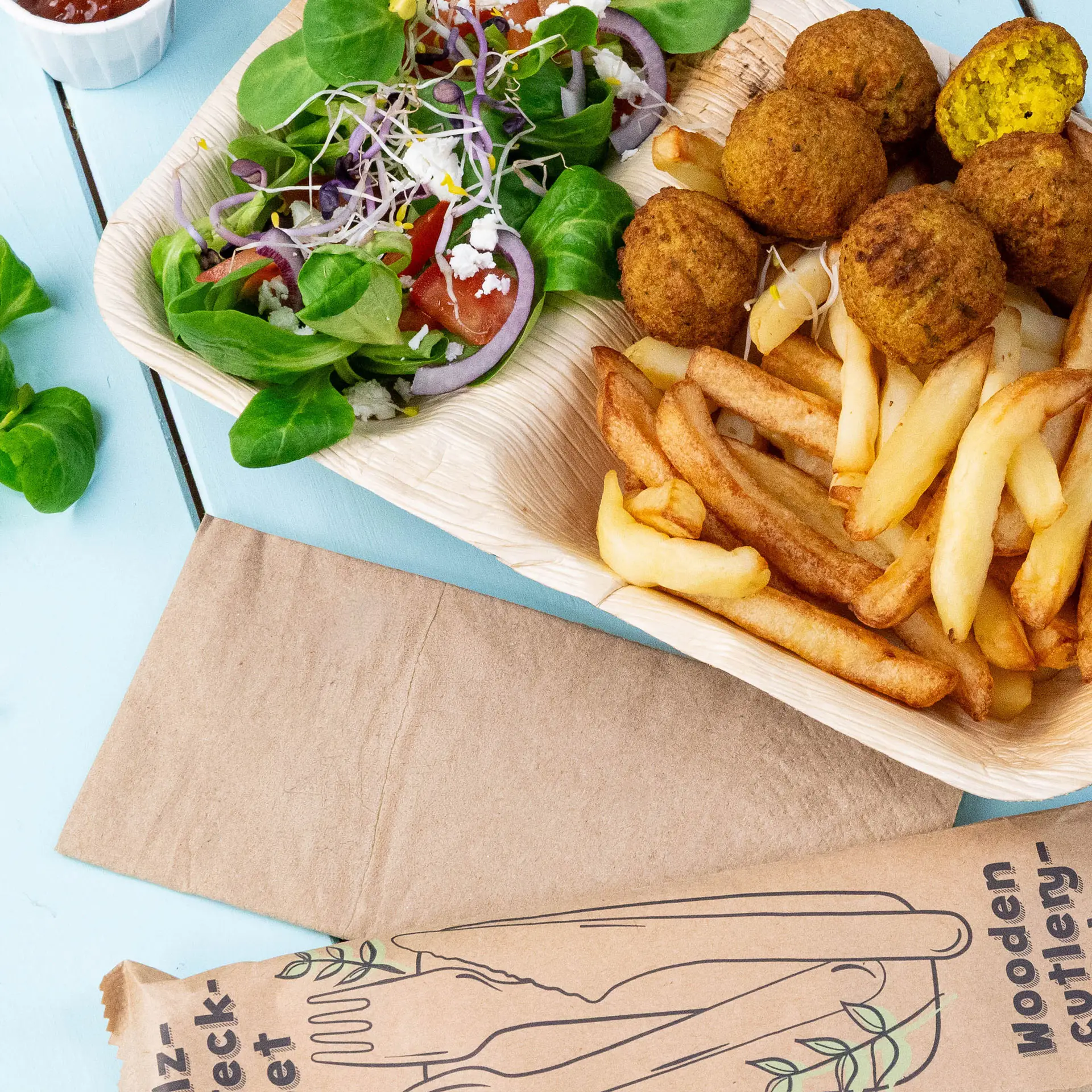 Obraz drewnianej tacy z kulkami falafel, frytkami i sałatką mieszana z zielenią, pomidorami i cebulą.