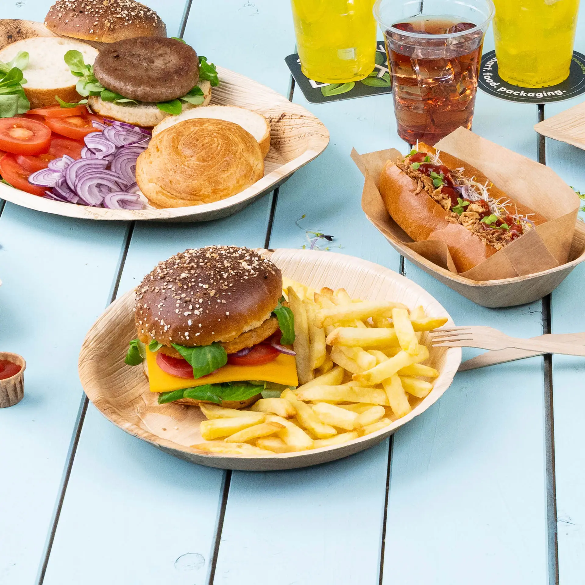 Okrągły talerz z liścia palmowego z hamburgerem z serem, sałatą i pomidorem, serwowany z frytkami na niebieskim stole.