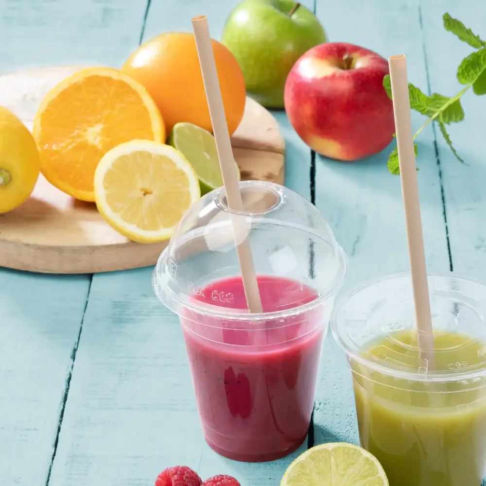 Dwa przezroczyste kubki z owocowymi smoothie, jeden różowy, drugi zielony, obok świeżych owoców na niebieskiej powierzchni.
