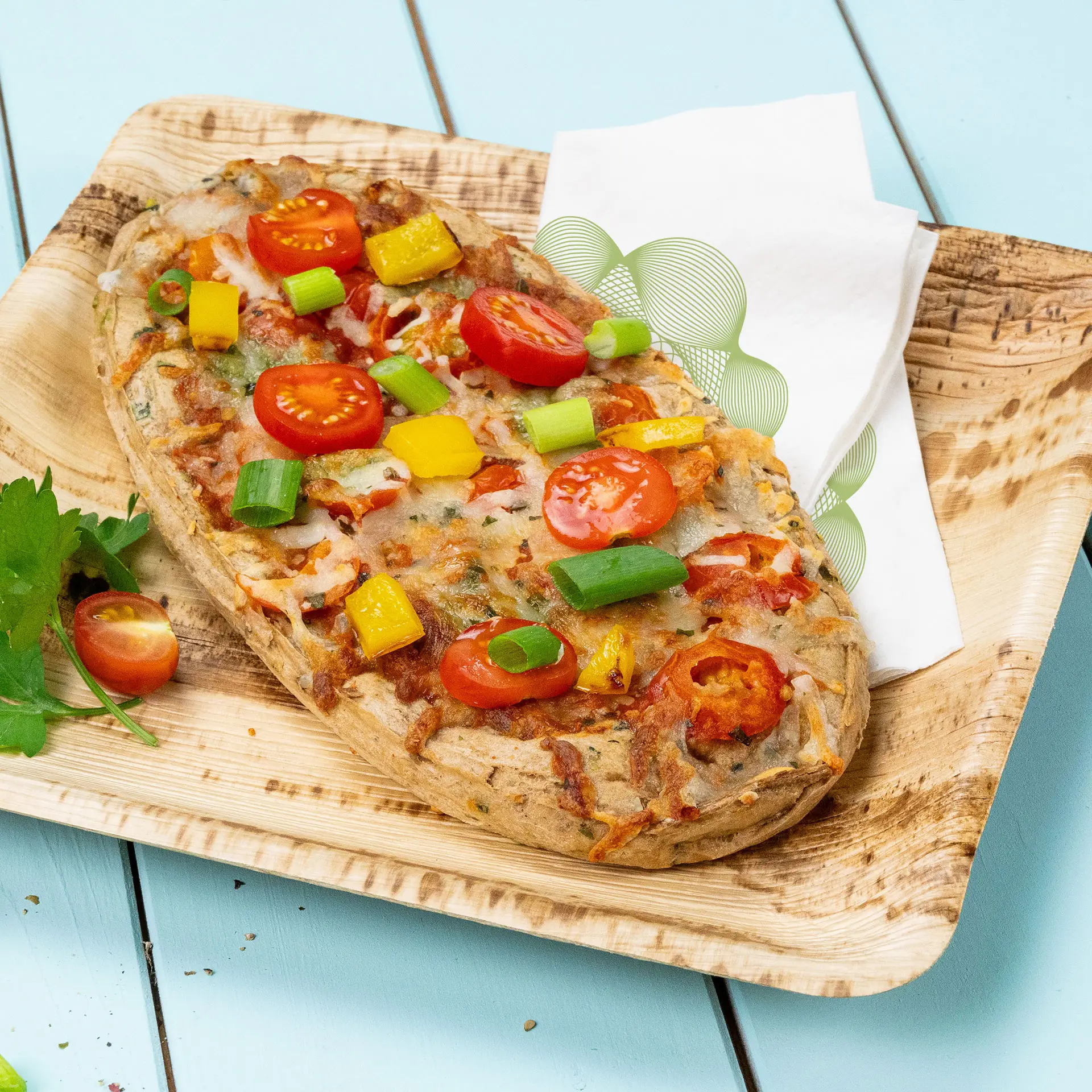 Pizza warzywna z pomidorkami koktajlowymi, dymką i żółtą papryką na drewnianym talerzu z serwetką.