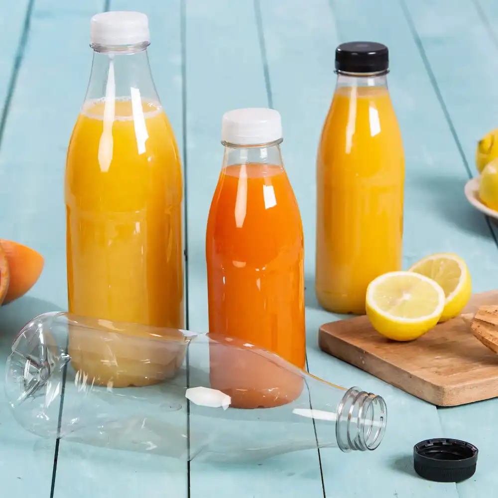 Trzy plastikowe butelki wypełnione żółtymi i pomarańczowymi sokami, jedna butelka leży, a obok leży cytryna i ciastka.