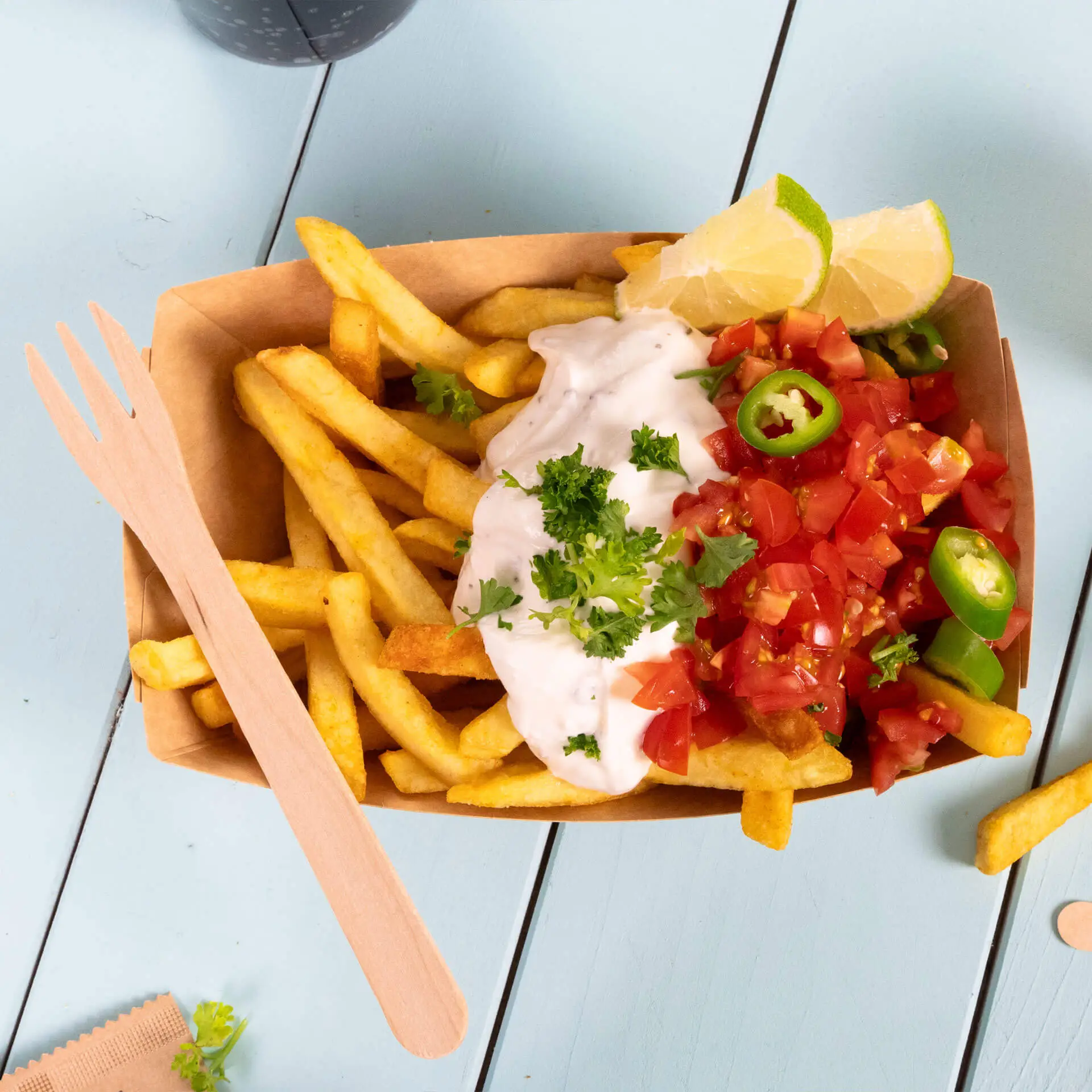 Widłak drewniany obok porcji frytek z kwaśną śmietaną, pomidorami, jalapeños i ćwiartkami limonki.