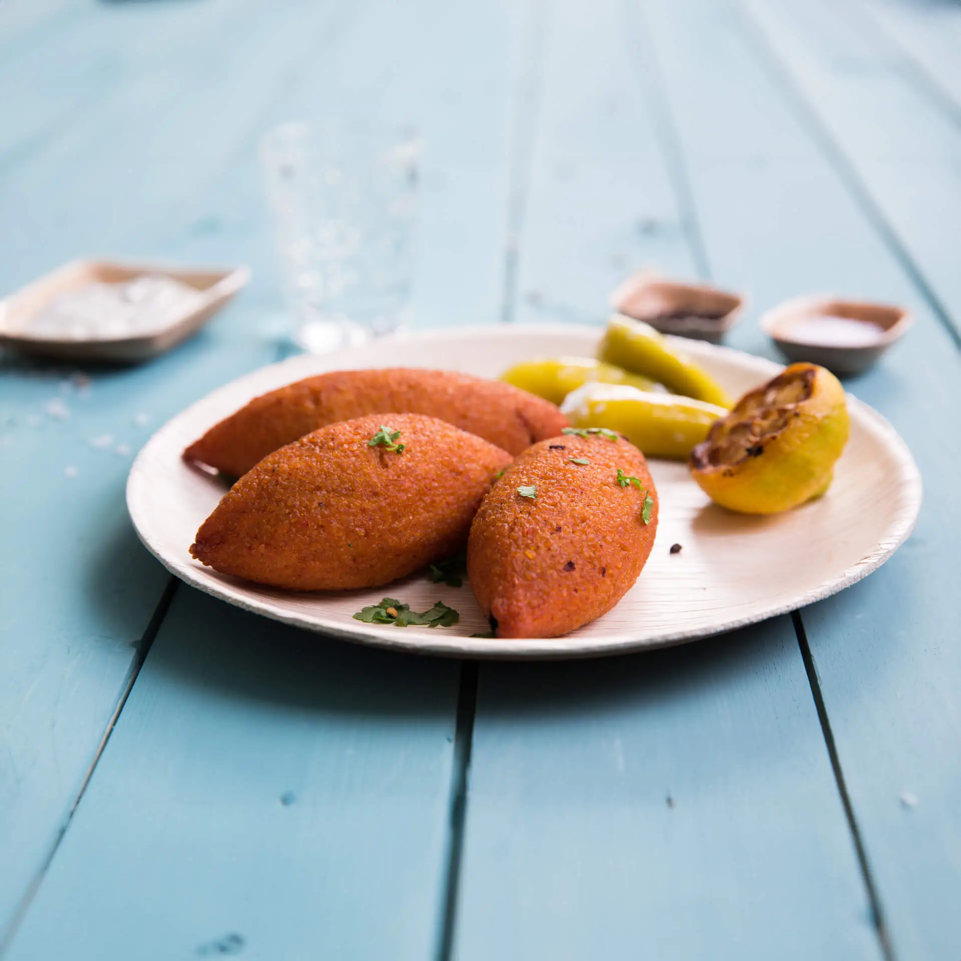 Trzy owalne talerze z liści palmowych z wąską krawędzią, z pomarańczowymi produktami spożywczymi, w towarzystwie zielonych papryk i grillowanej plastry cytryny.