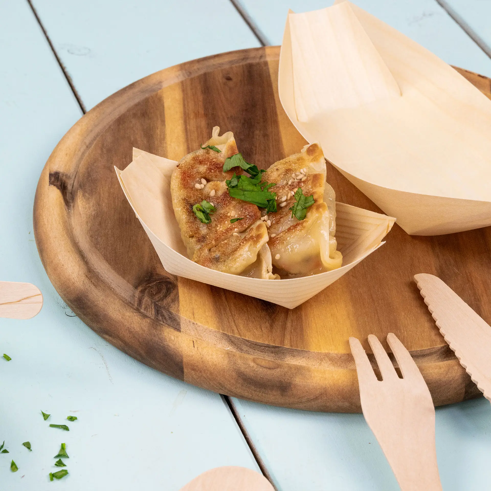 Dwa złocisto-brązowe pierożki w drewnianej łódce na drewnianym talerzu; udekorowane zielonymi ziołami; tle o naturalnej teksturze.