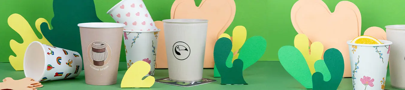 Obraz różnych personalizowanych kubków z kolorowymi wycinankami na zielonym tle.