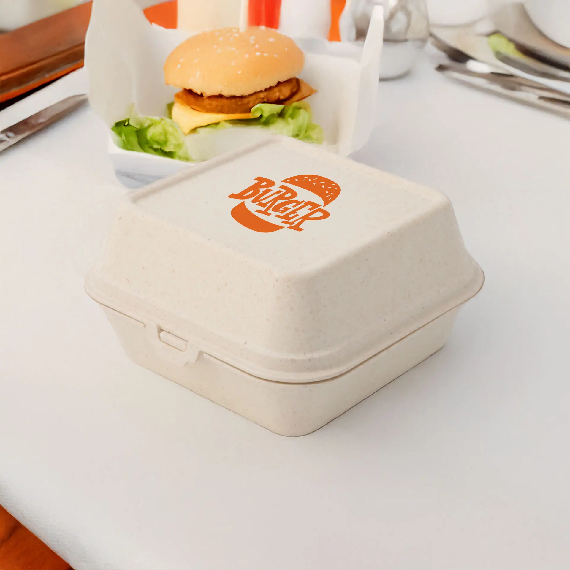 Kremowa prostokątna pudełko na burger z nadrukowanym logo, umieszczona na stole obok burgera i sałaty.