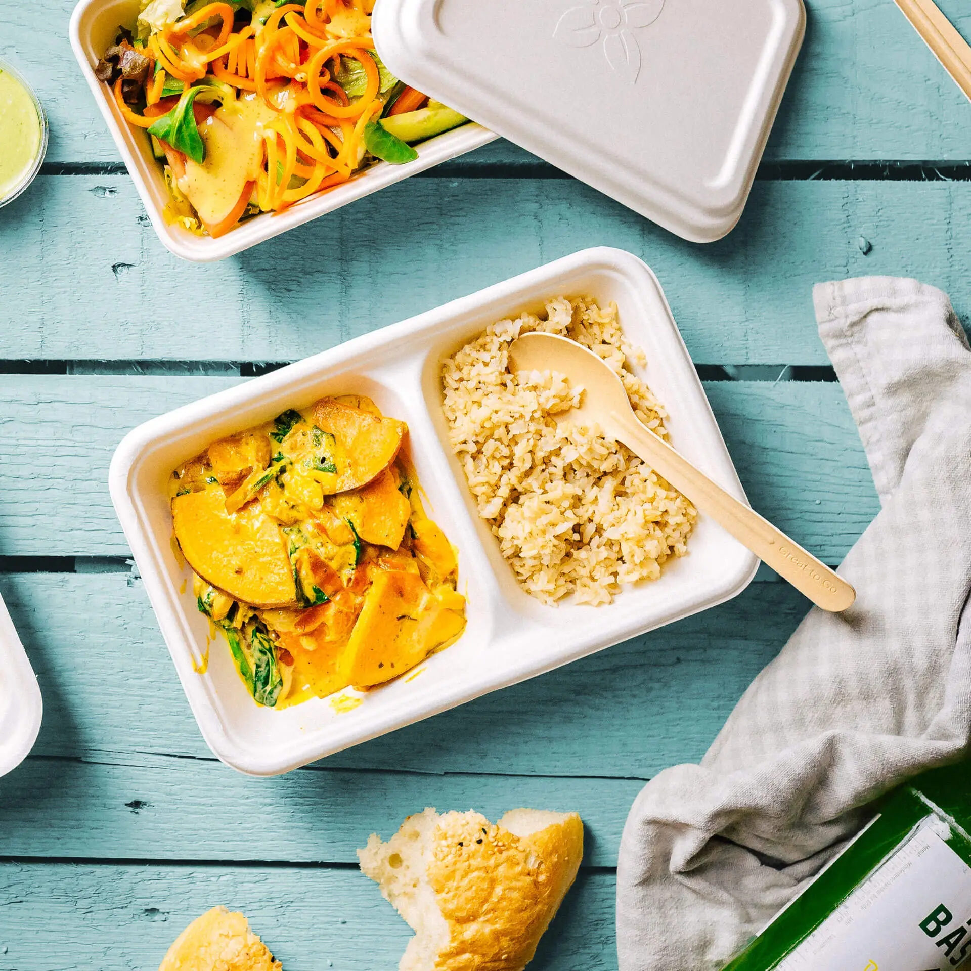 Jedna biodegradowalna miska z trzciny cukrowej z dwoma przegrodami; zawiera żółte danie warzywne i brązowy ryż, z drewnianą łyżką.