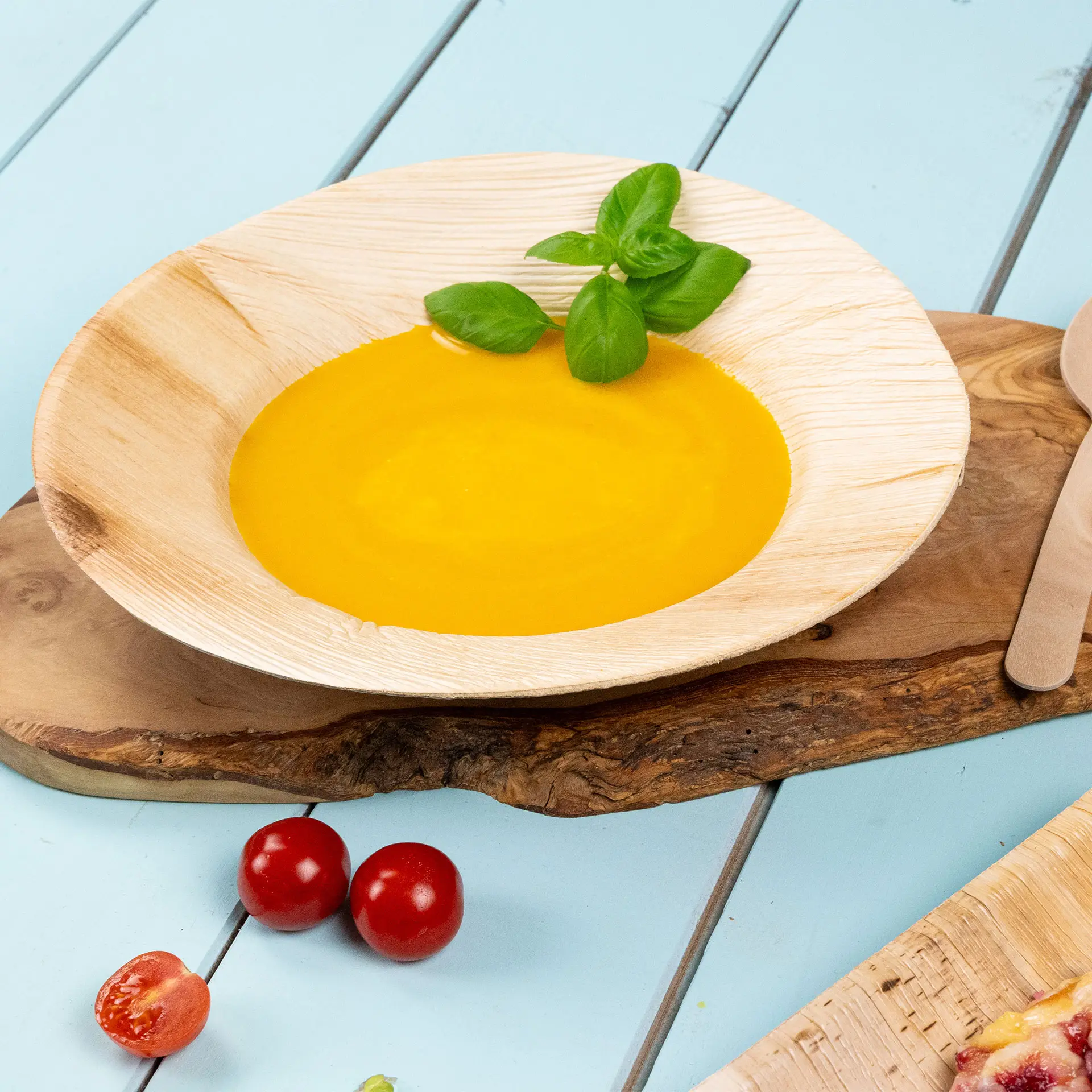 Talerz z liści palmowych, średnica 23 cm, wypełniony złotą zupą i ozdobiony liśćmi bazylii; obok koktajlowe pomidory.