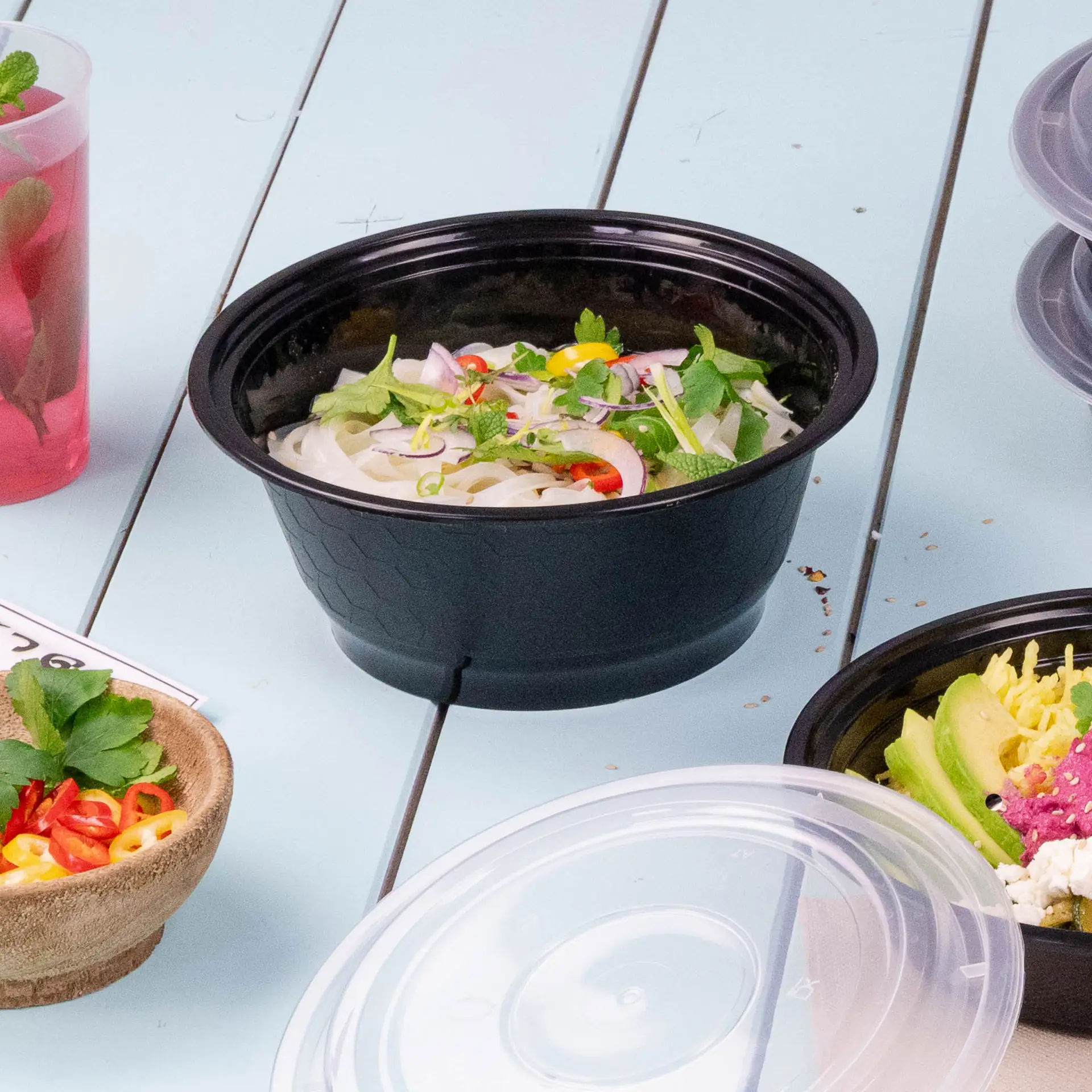 Czarny pojemnik wielokrotnego użytku wypełniony makaronem, udekorowany świeżymi ziołami i chili; inne produkty spożywcze w pobliżu.