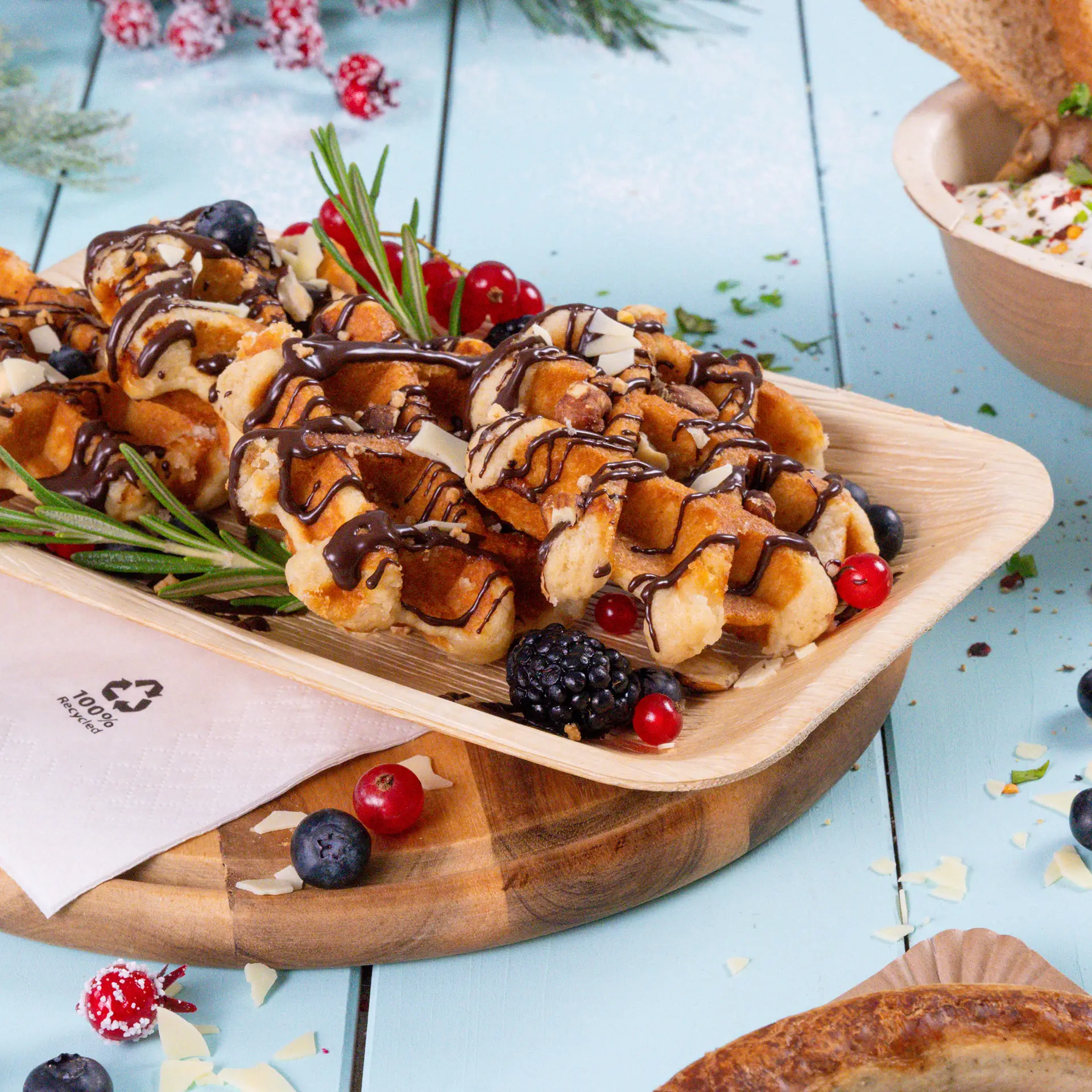 Pyszne wafle polane czekoladą i ozdobione jagodami, podane na talerzu z liści palmowych.