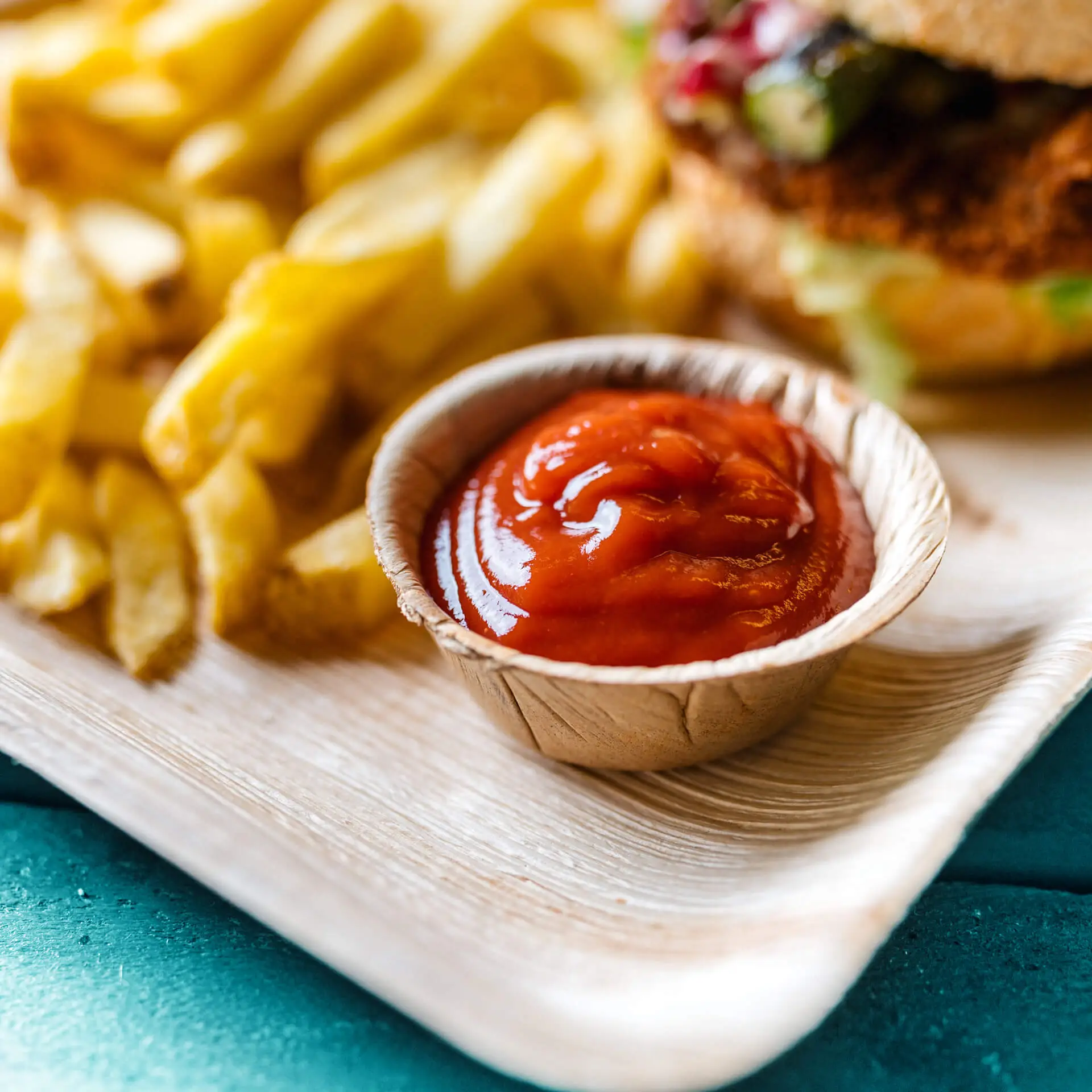 Mini miska z liści palmowych z ketchupem, w tle frytki na tacy.