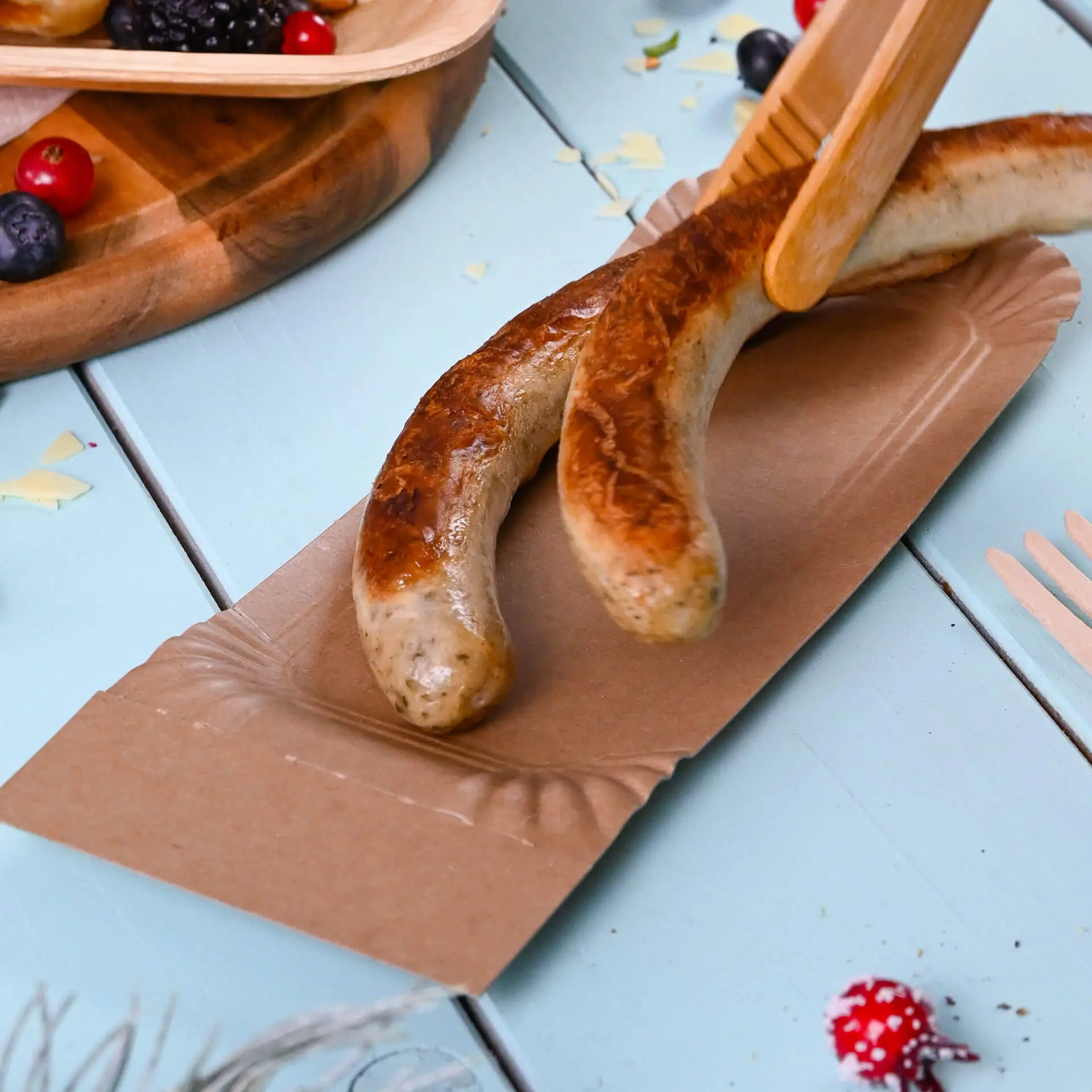 Dwie grillowane kiełbaski na odrywanym kartonowym talerzu; talerz jest brązowy i prostokątny, odpowiedni do serwowania przekąsek.