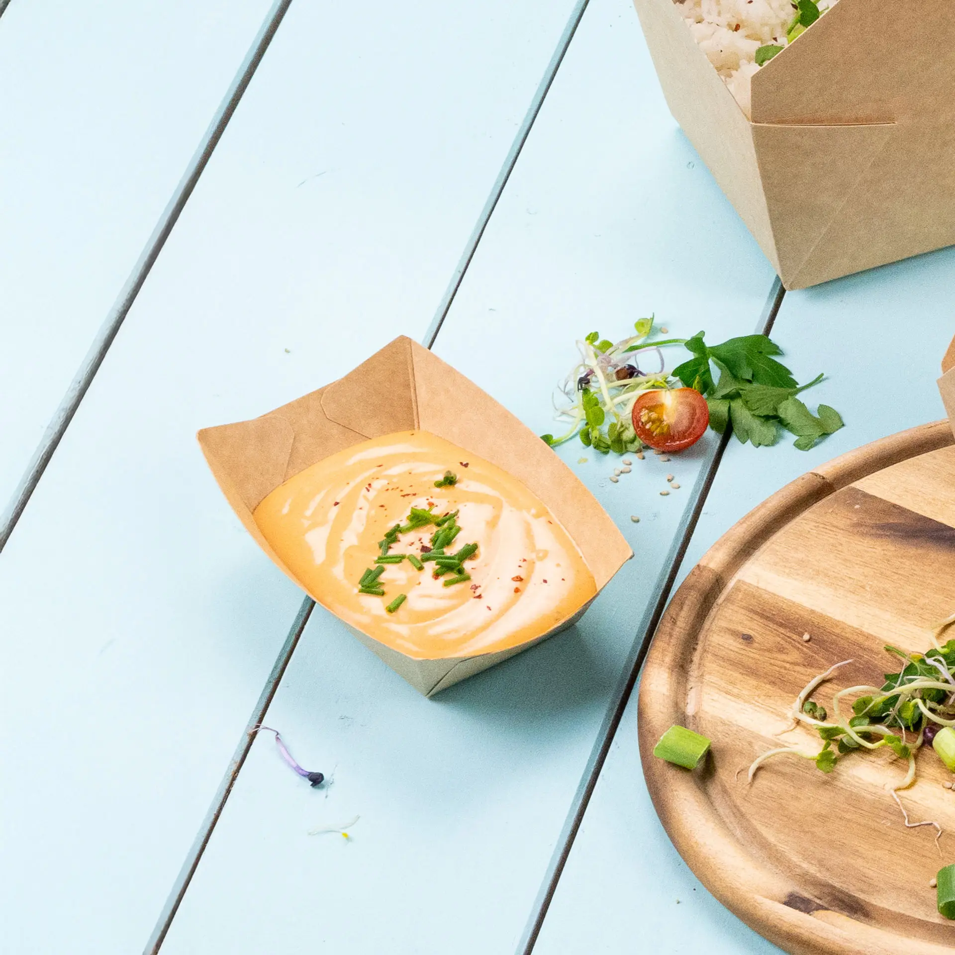 Brąska taca na przekąski z kremowym sosem i posiekanymi ziołami; widoczne kilka warzyw oraz część talerza.